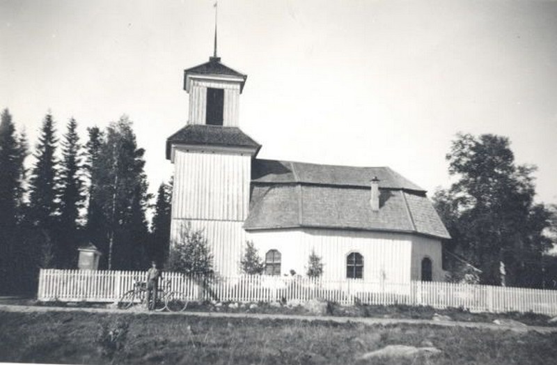Ett äldre svartvitt fotografi av Gålsjö kapell. Framför kapellet står en man med cykel