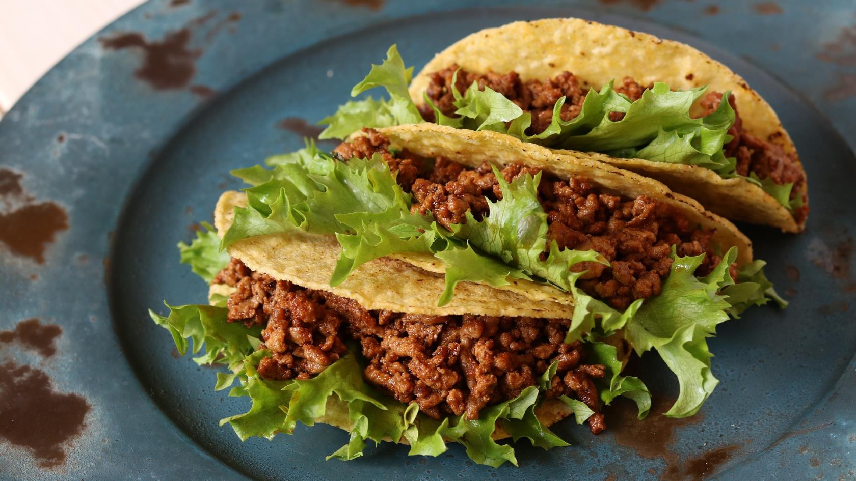 En blå tallrik med tre köttfärsfyllda tacoskal.