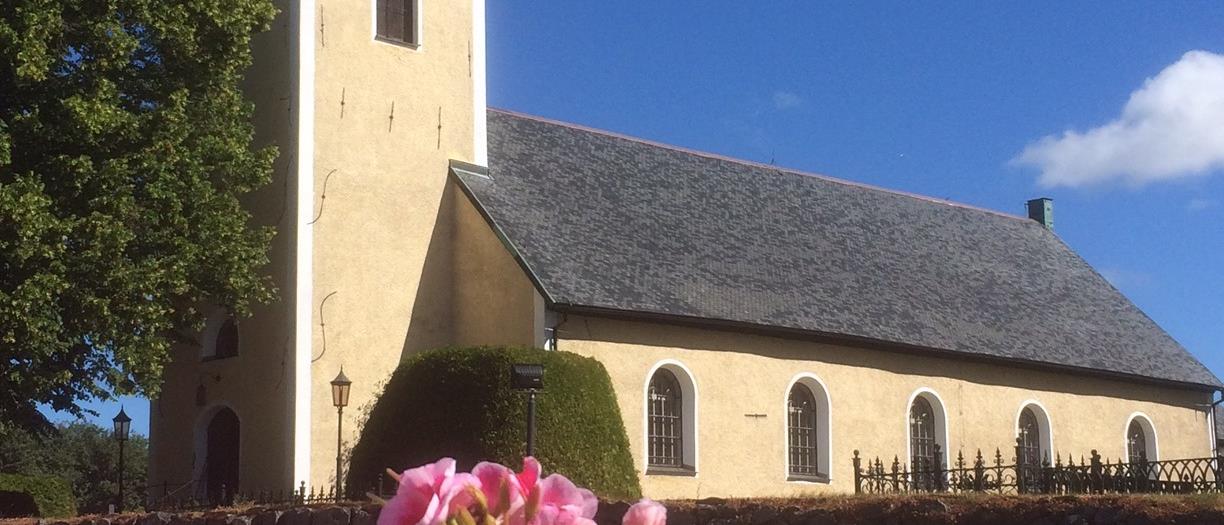 Snavlunda kyrka en sommardag, i förgrunden syns rosa pelargoner