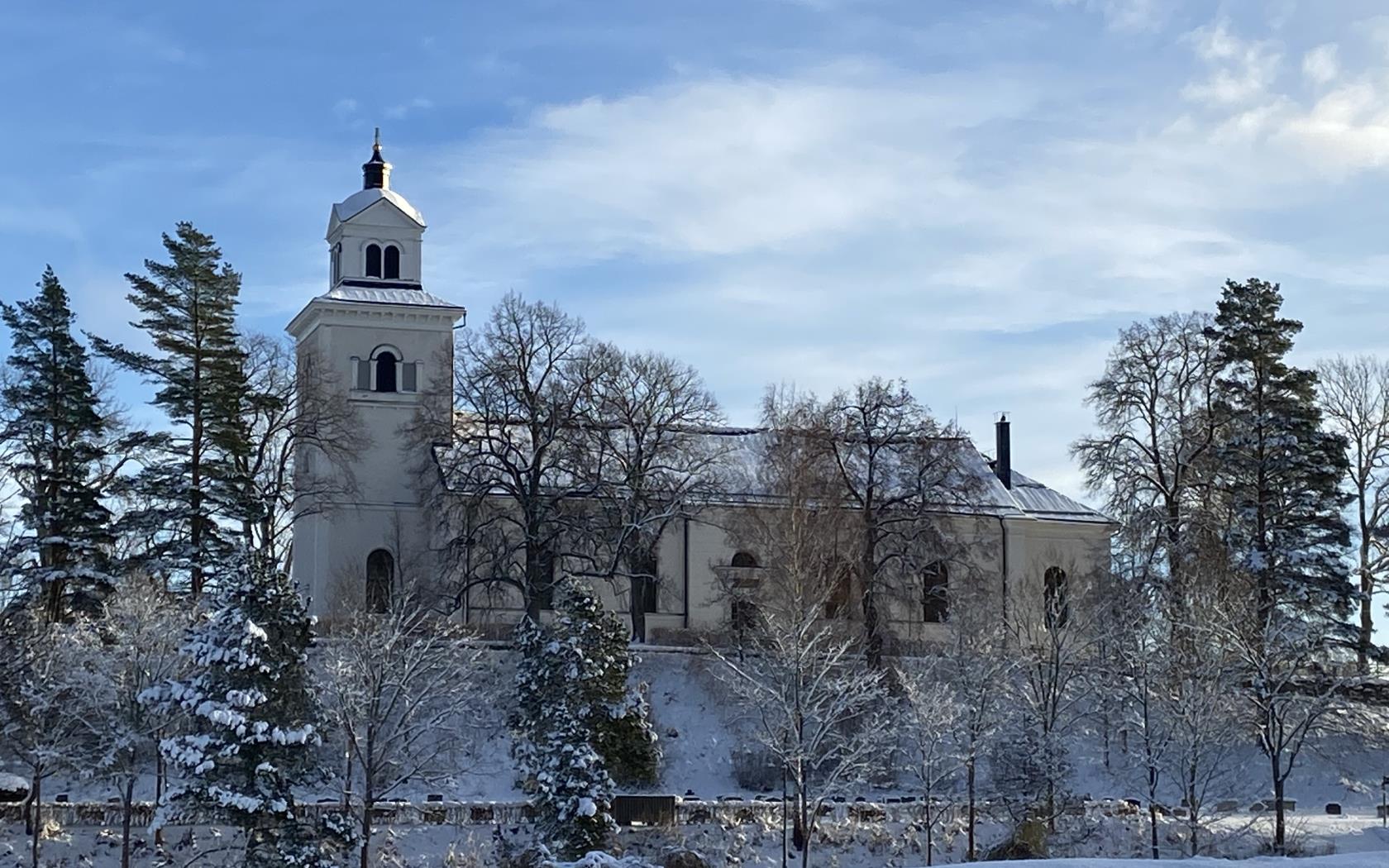 Hammars kyrka ligger på en höjd omgiven av träd, det är en vacker vinterdag med snö. 