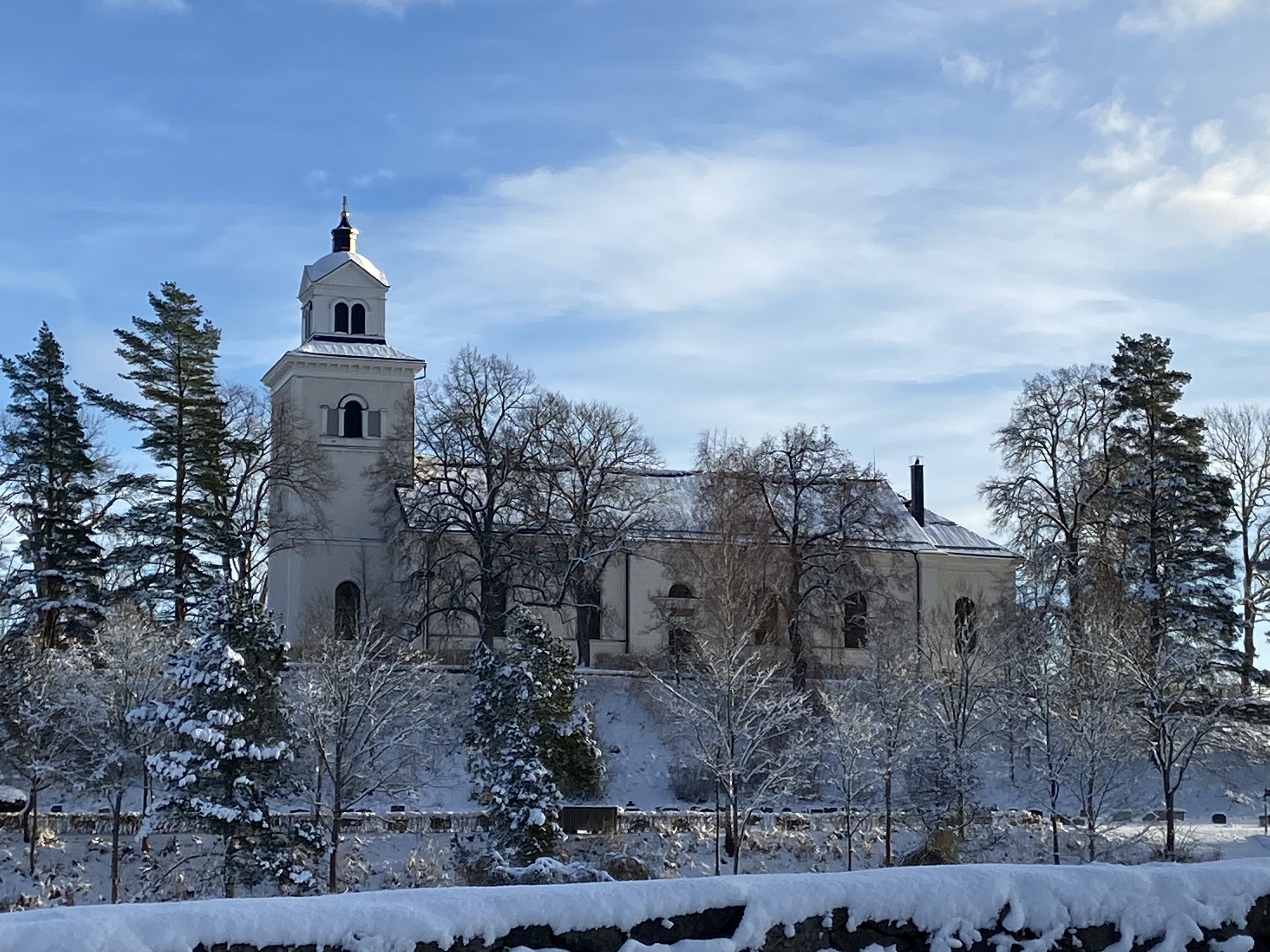 Hammars kyrka ligger på en höjd omgiven av träd, det är en vacker vinterdag med snö. 