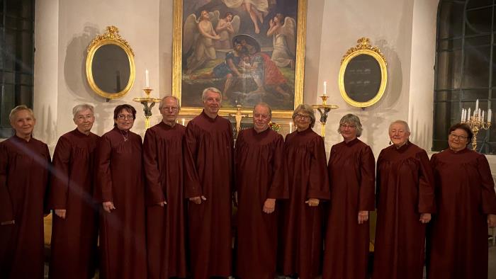 Lerbäcks kyrkokör framför altaret i Lerbäcks kyrka. De är klädda i vinröda körkåpor.