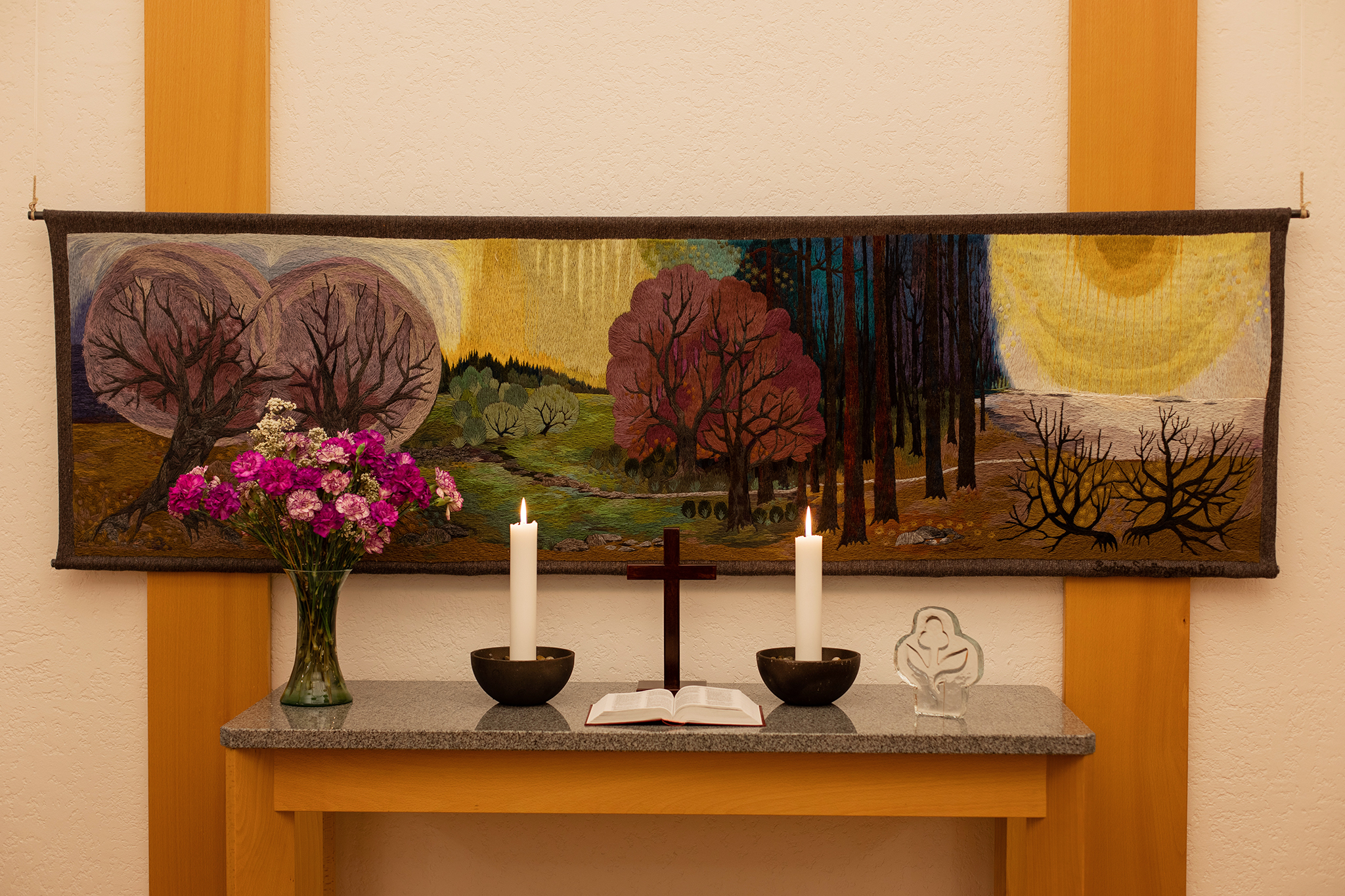 Ett altare med två ljus och en bukett blommor. Bakom altaret en altartavla.