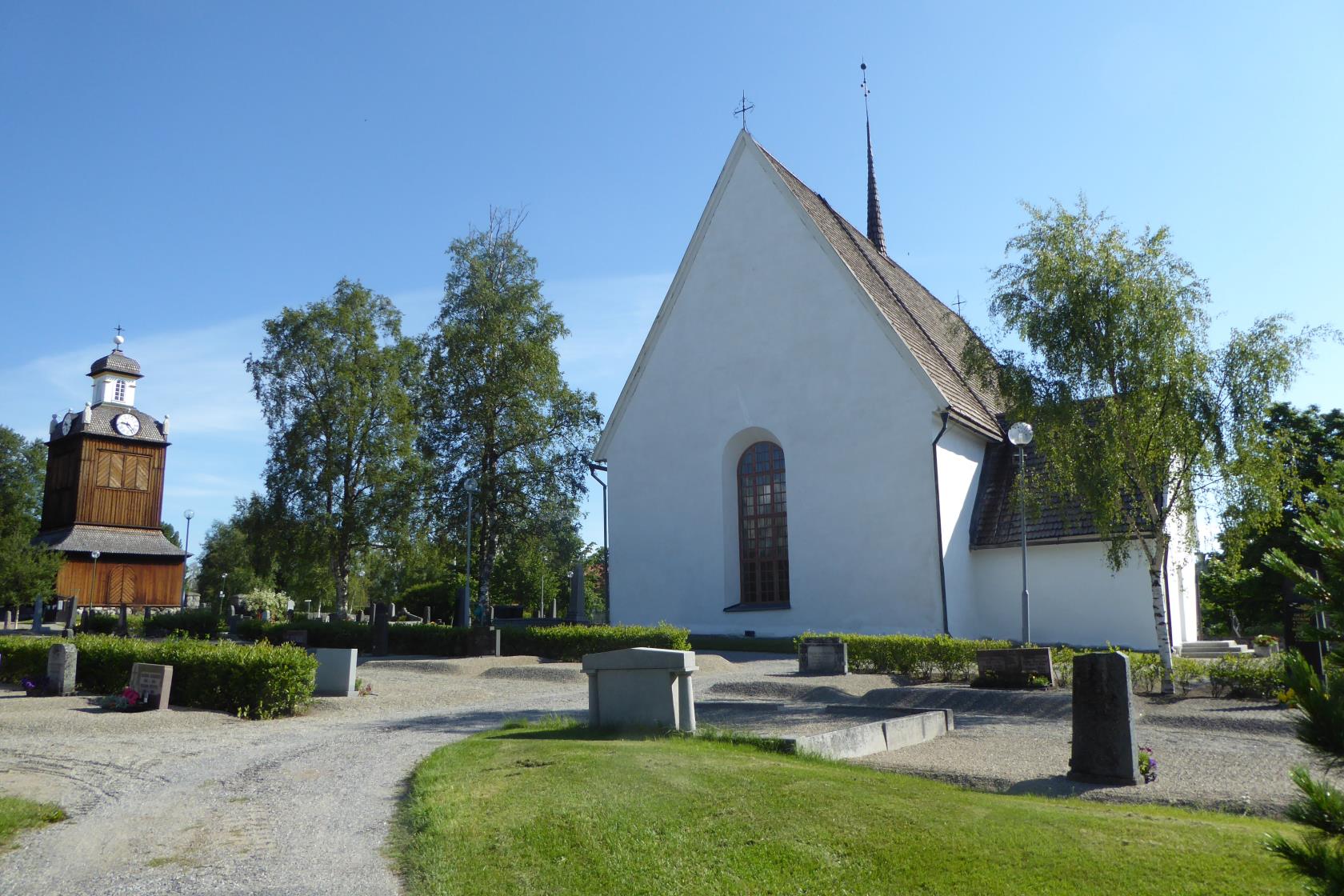 Vit kyrkobyggnad, klockstapel och gravstenar