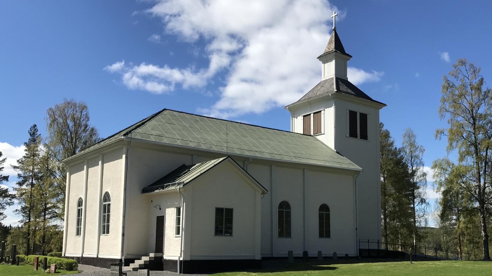 Exteriörbild av Trehörningsjö kyrka med grönskande bakgrund.