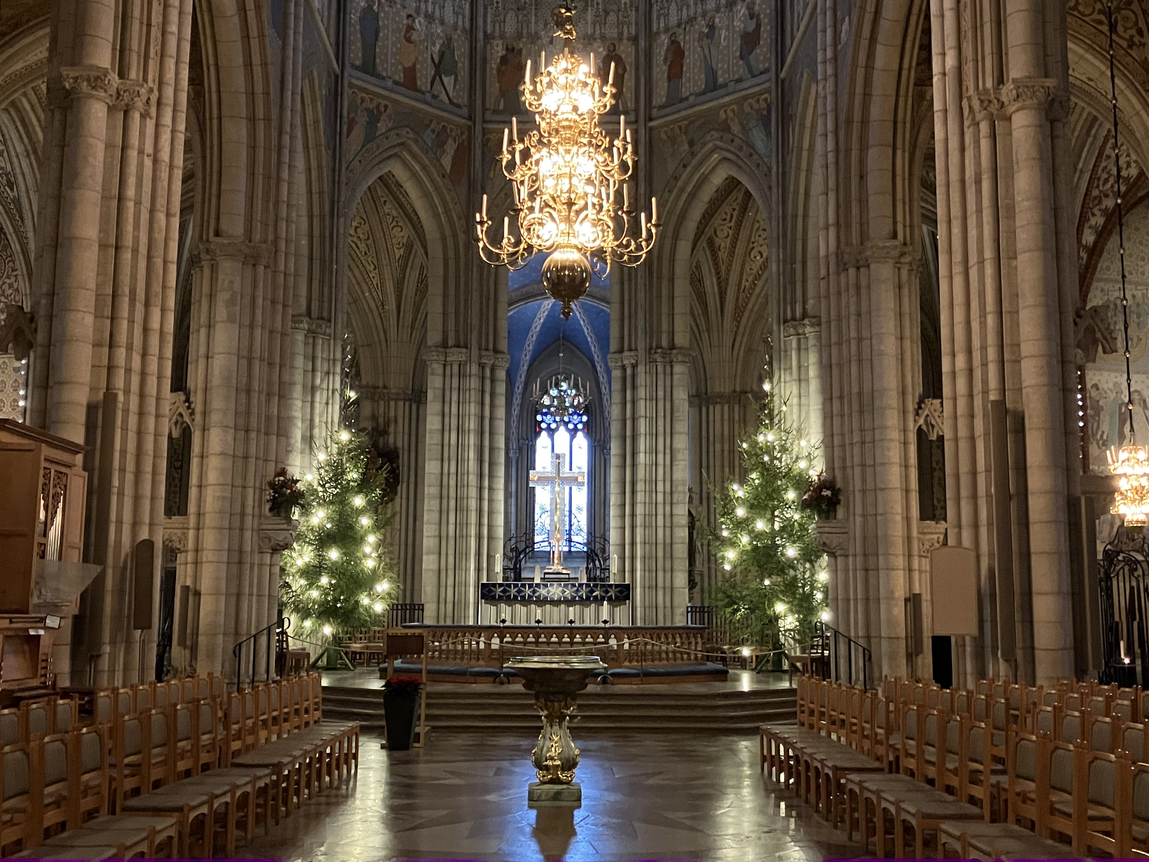 Högkoret i Uppsala domkyrka med två julgranar fulla av lampor, med kristallkorset i mitten.