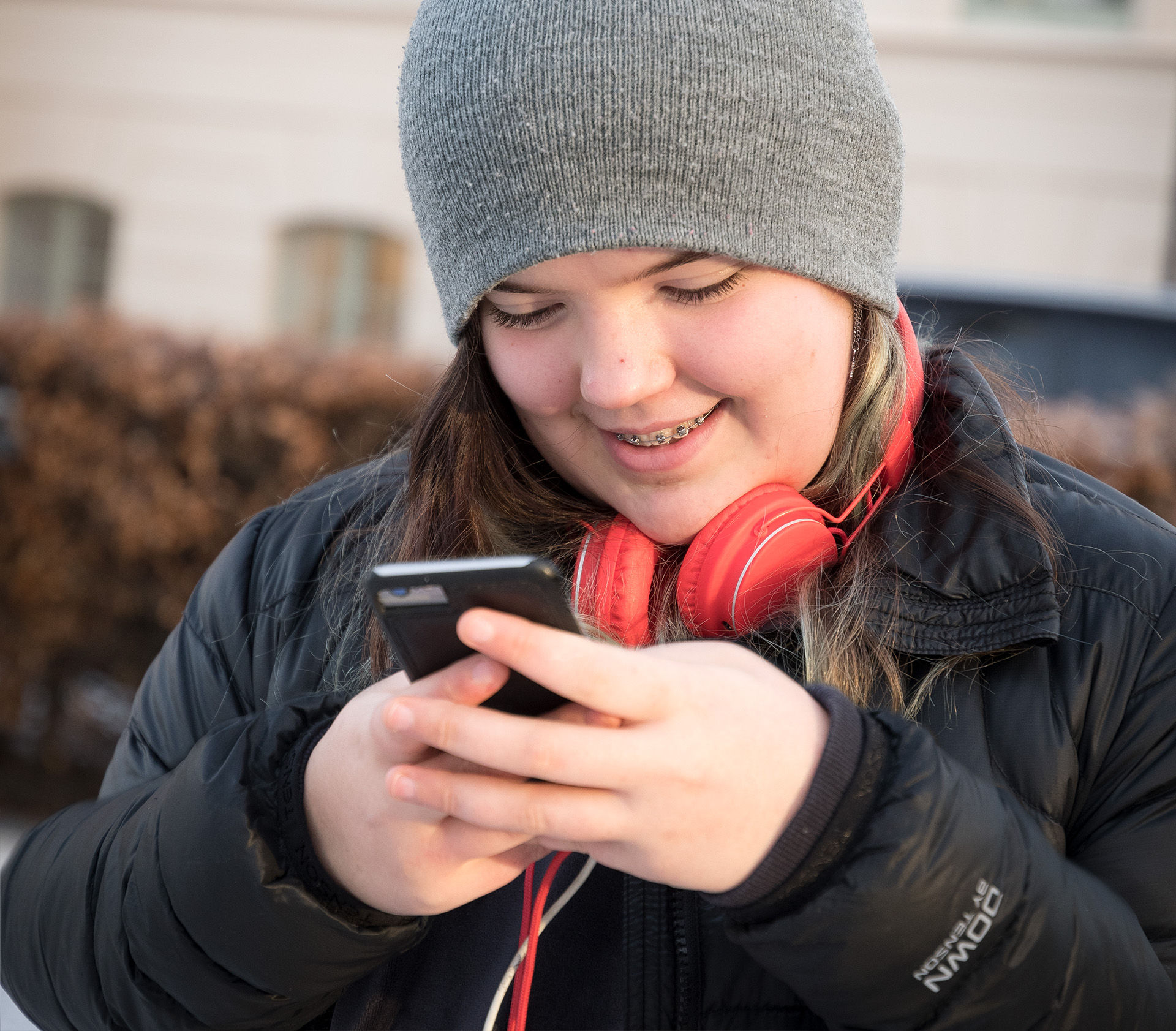 En ung tjej med röda hörlurar knappar in ett nummer på mobiltelefonen.