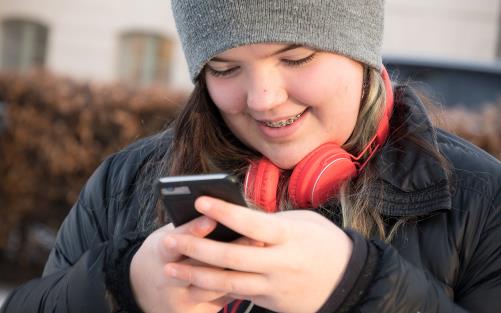 En ung tjej med röda hörlurar knappar in ett nummer på mobiltelefonen.