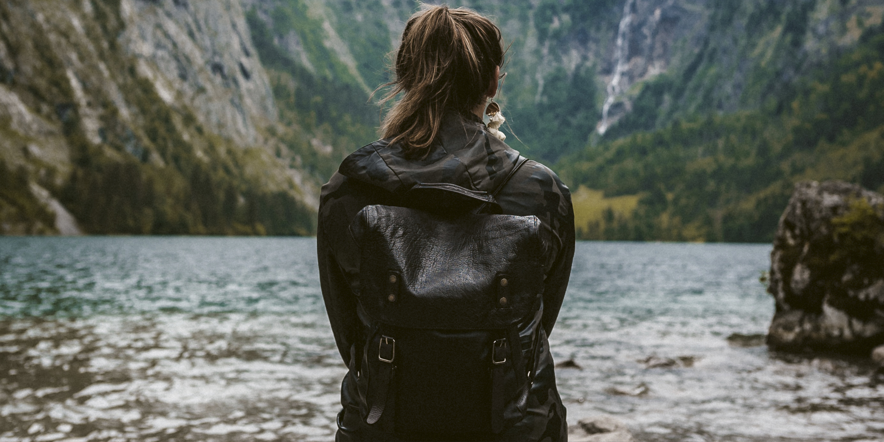 Ung kvinna tittar ut över en sjö med omgivande berg. 