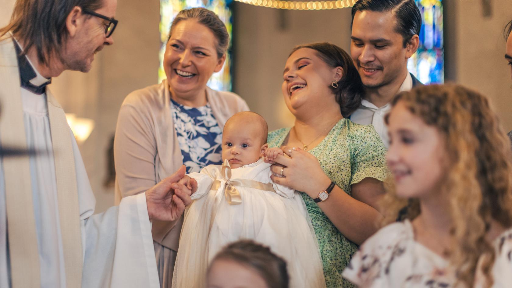 Familj skrattar tillsammans med präst från Svenska kyrkan under barndop