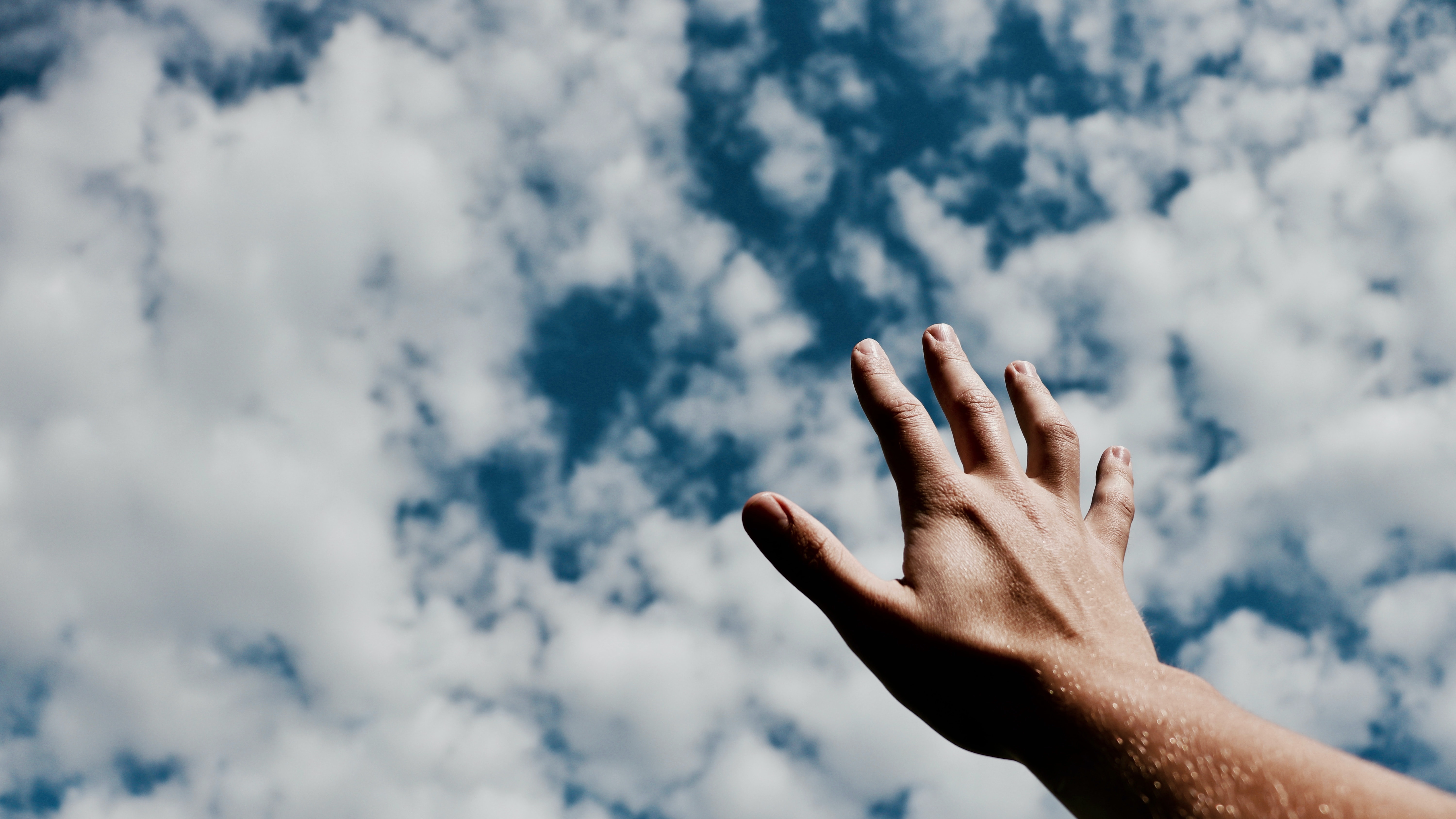 Hand som sträcker sig mot molnig himmel. 