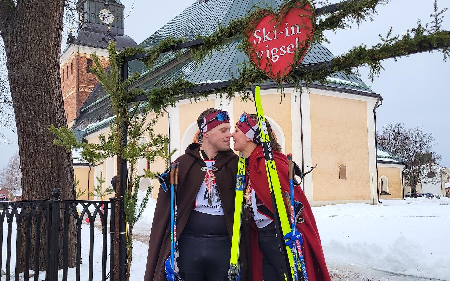 Nygift par ståendes med längdskidor vid målgången av Vasaloppet 2024.