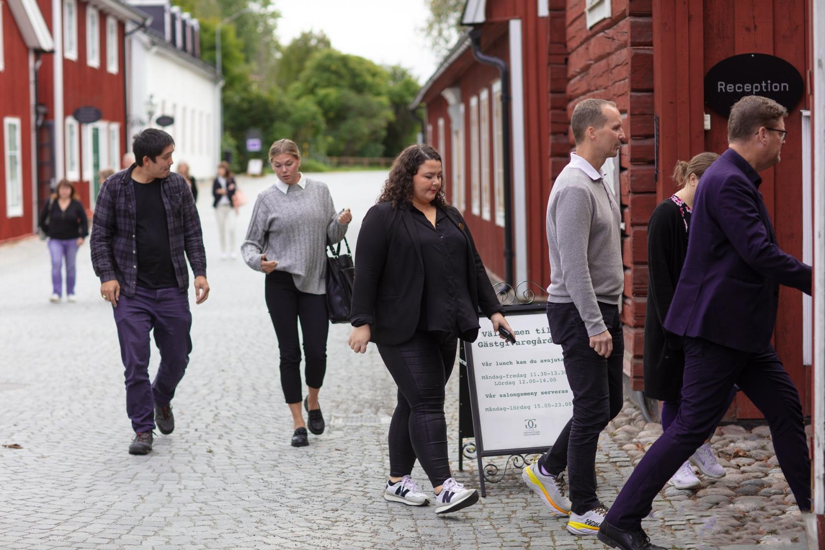 Enn antal personer som går på en mindre gata. De är på väg in i ett hus.