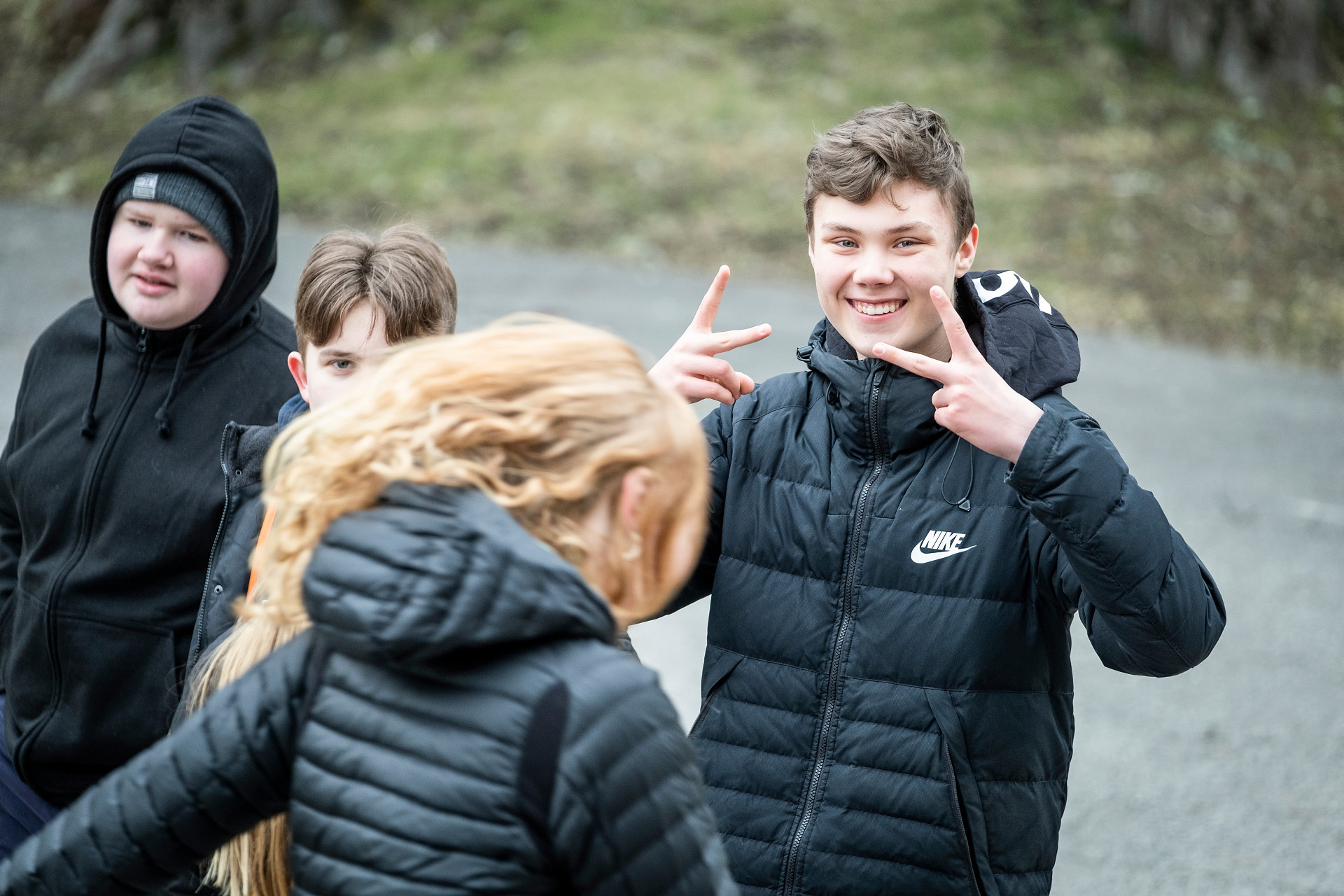 En grupp med ungdomar, en pojke ler mot kameran och gestikulerar med händerna.