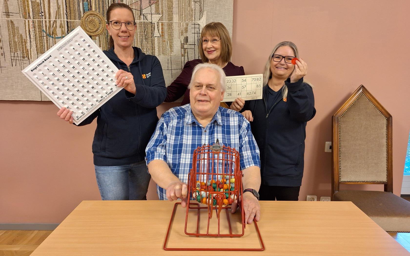 Fyra personer sitter och står runt ett bord med bingosnurran och bingobrickor