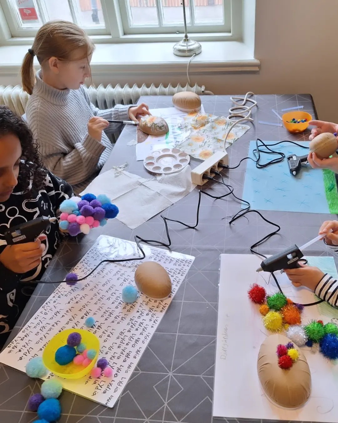 3 barn sitter och pysslar, bordet är fullt av pyssel.