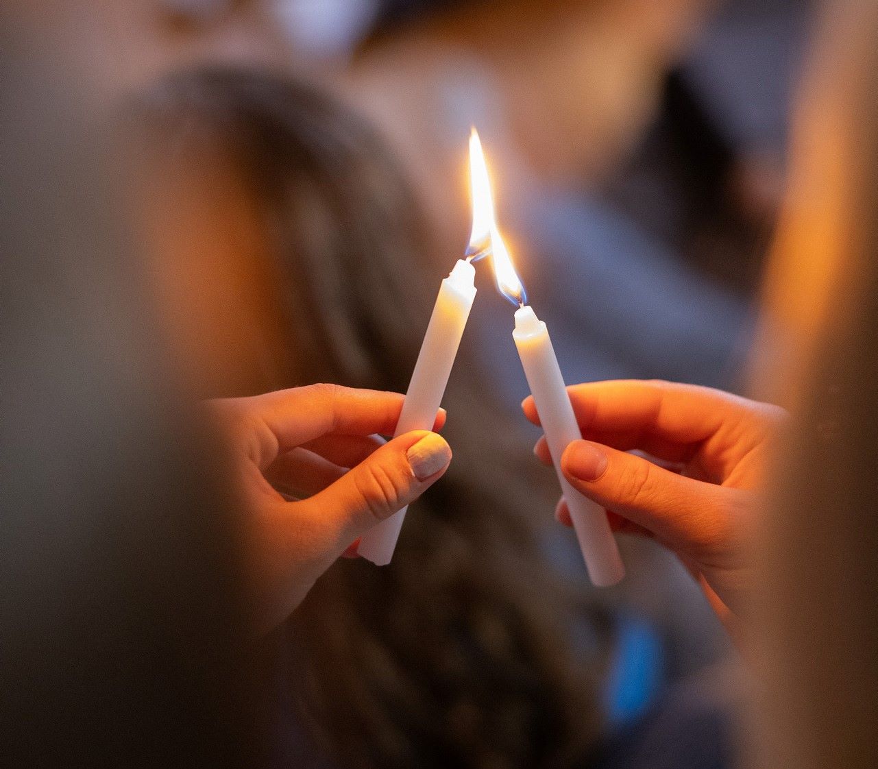 Två personer håller i varsitt stearinljus. Den ena tänder sitt ljus med hjälp av det andra ljusets låga.