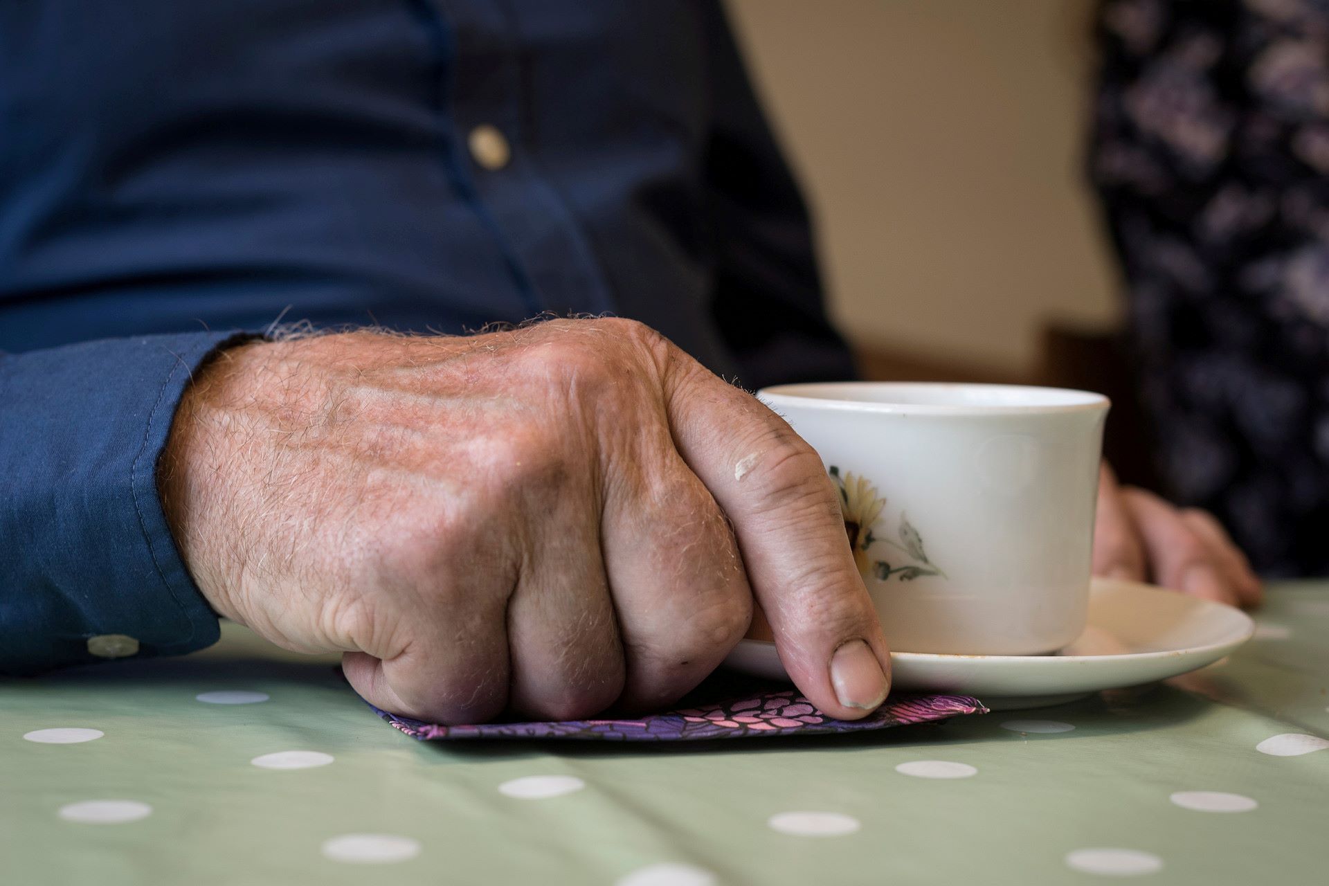 Närbild på en äldre mans hand som håller i en kaffekopp.