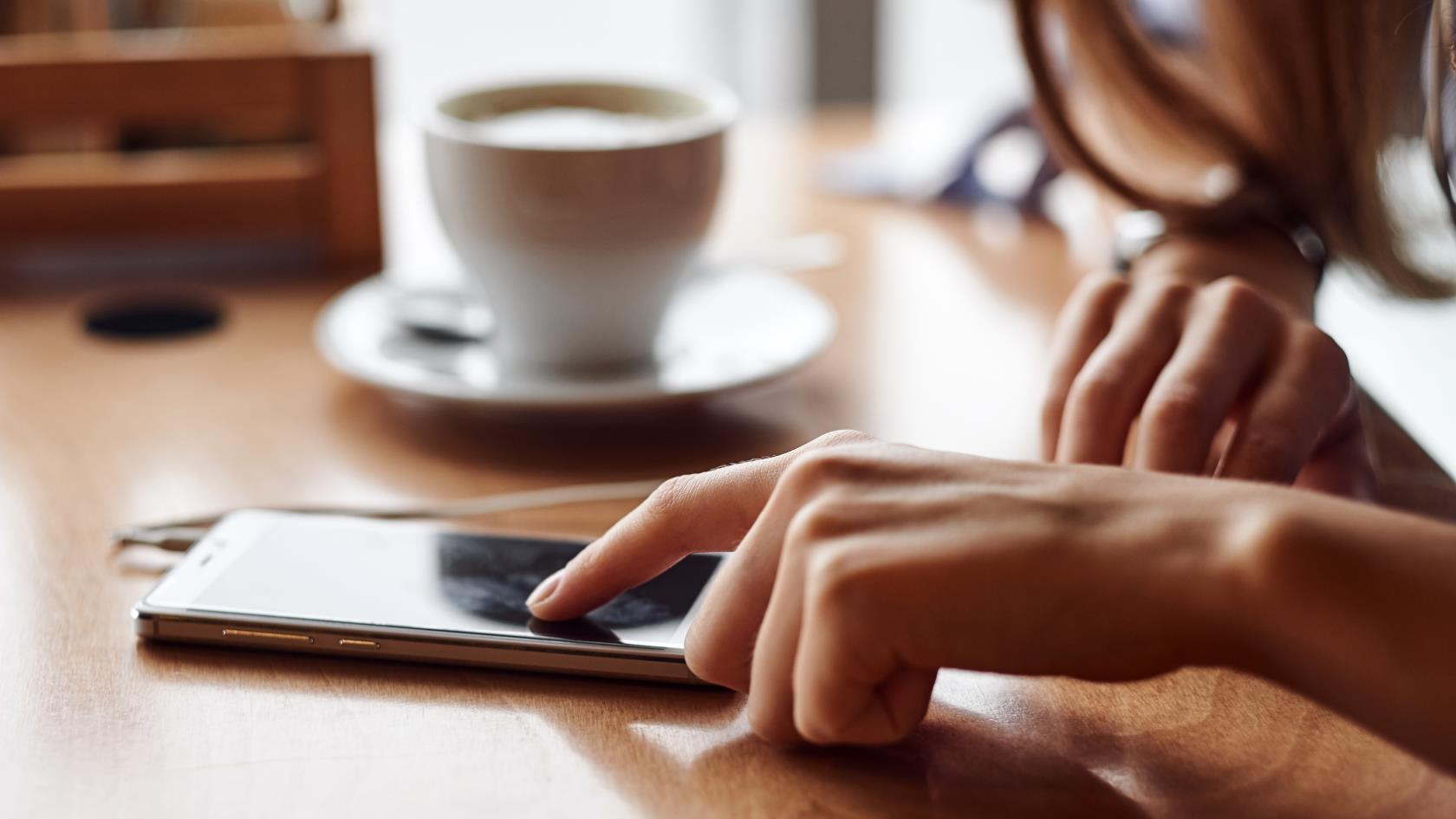 En person med en kopp kaffe som använder sin smartphone.