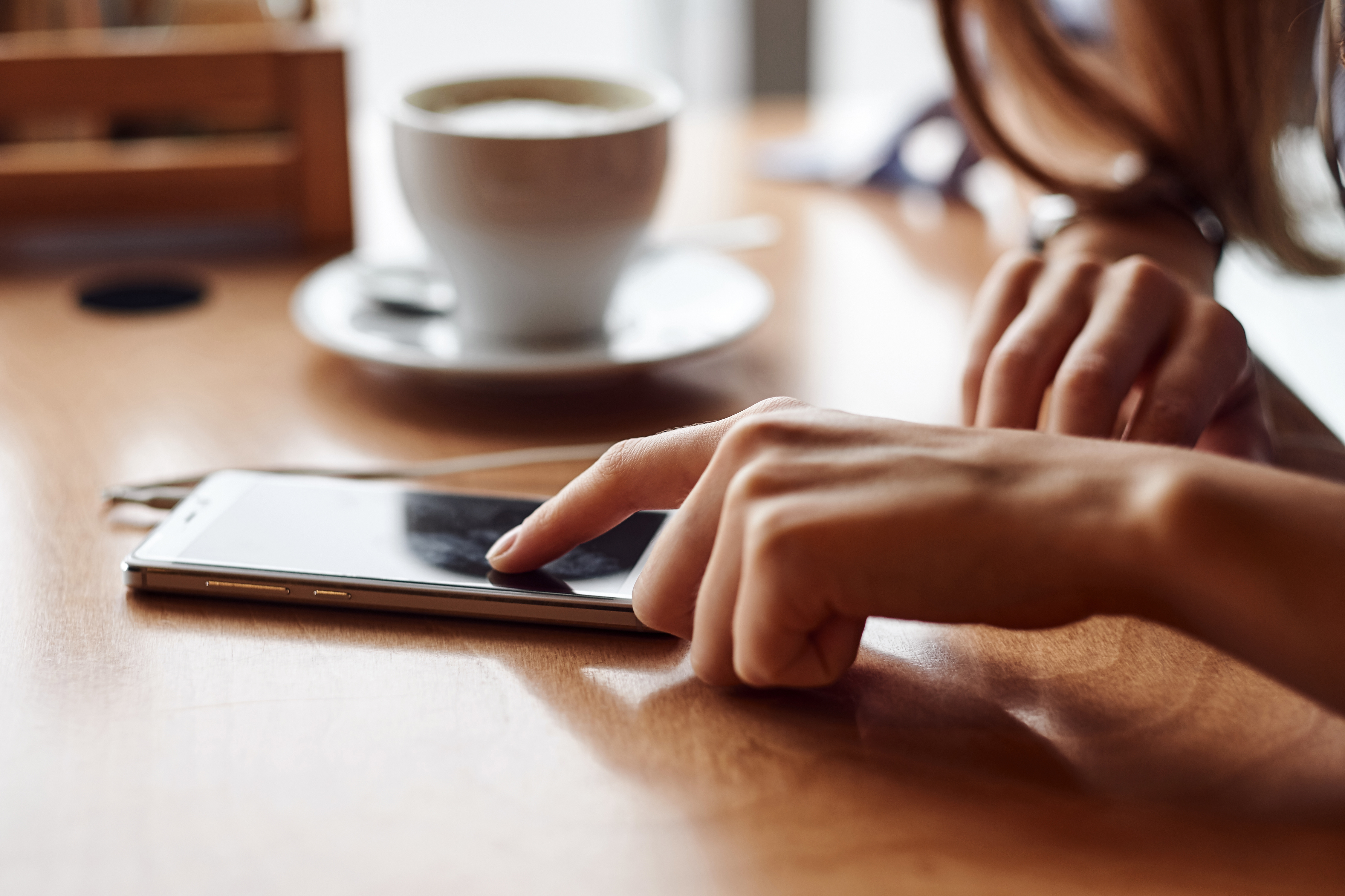 En person med en kopp kaffe som använder sin smartphone.