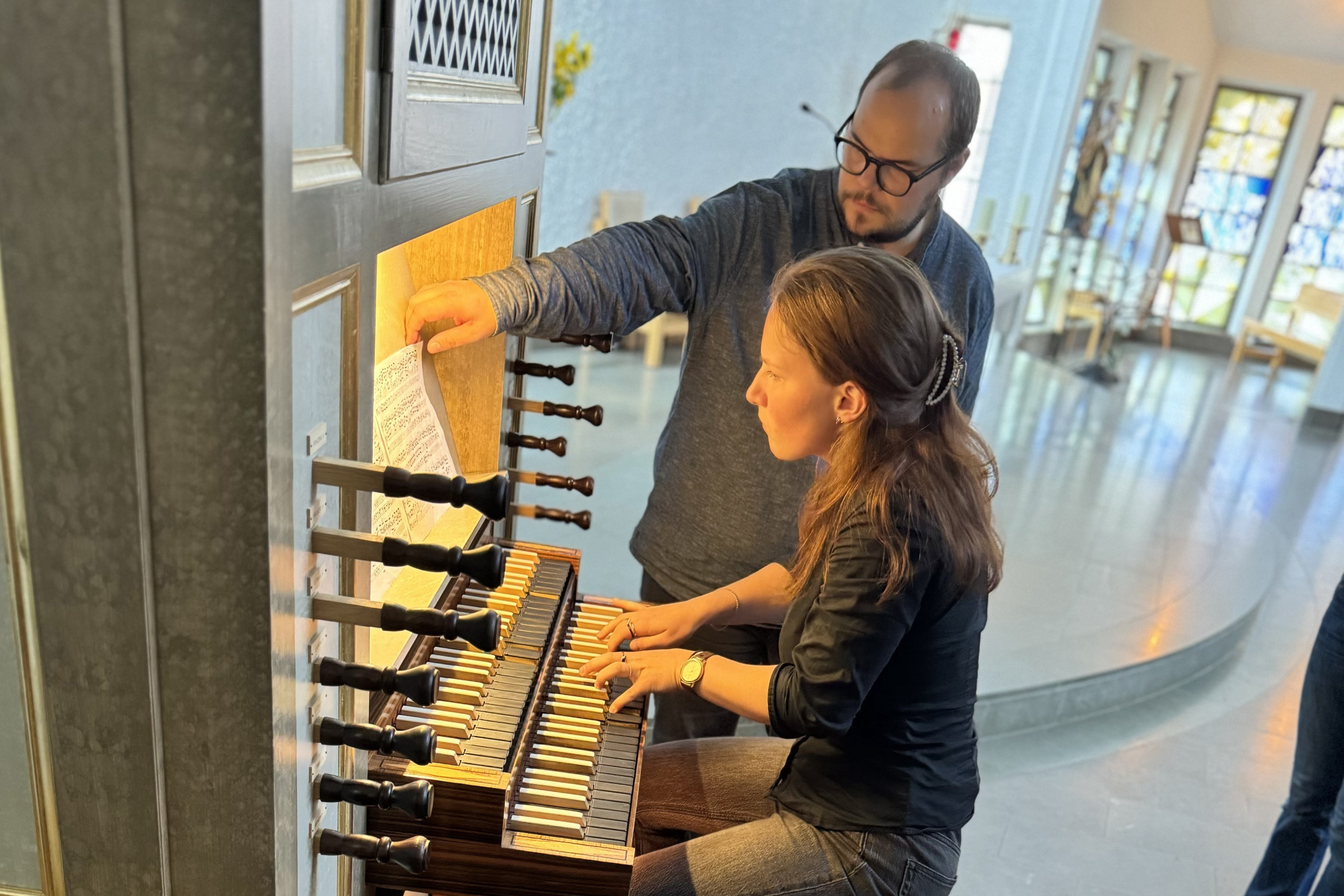 En kvinna spelar på en orgel, en man vänder noter