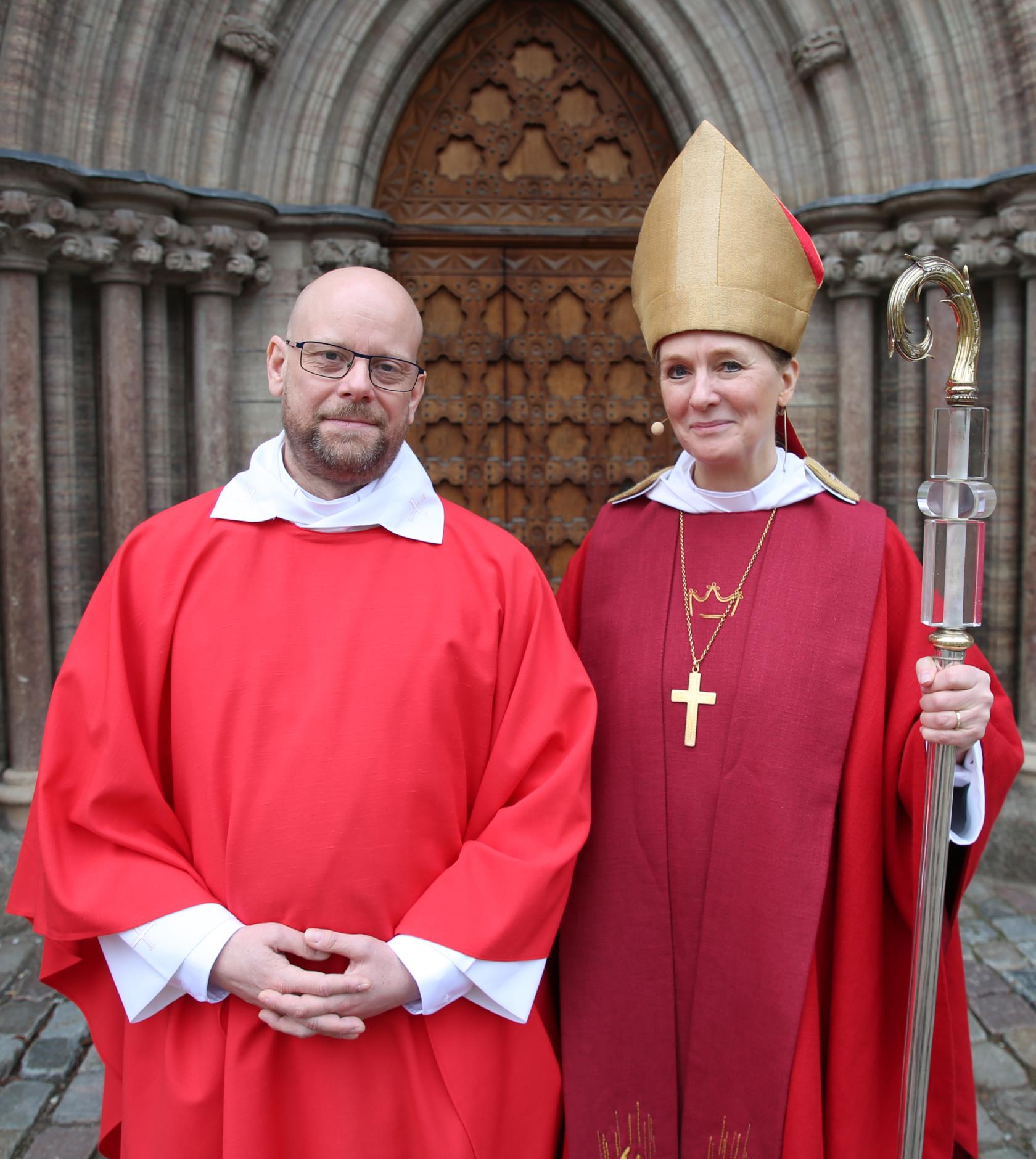 En nyvigd präst och en biskop framför en kyrkport.