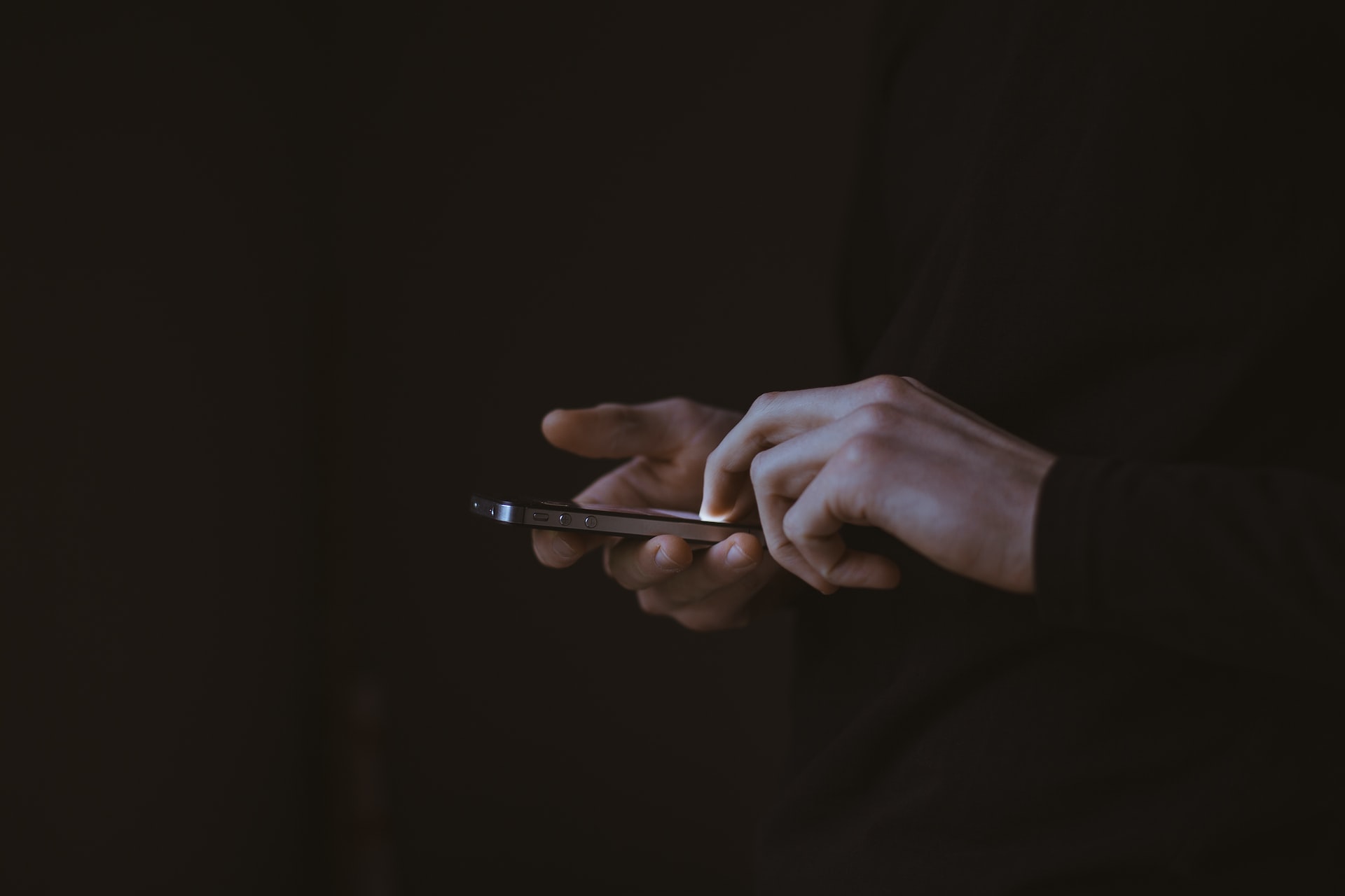 Två händer håller en smartphone i mörkret
