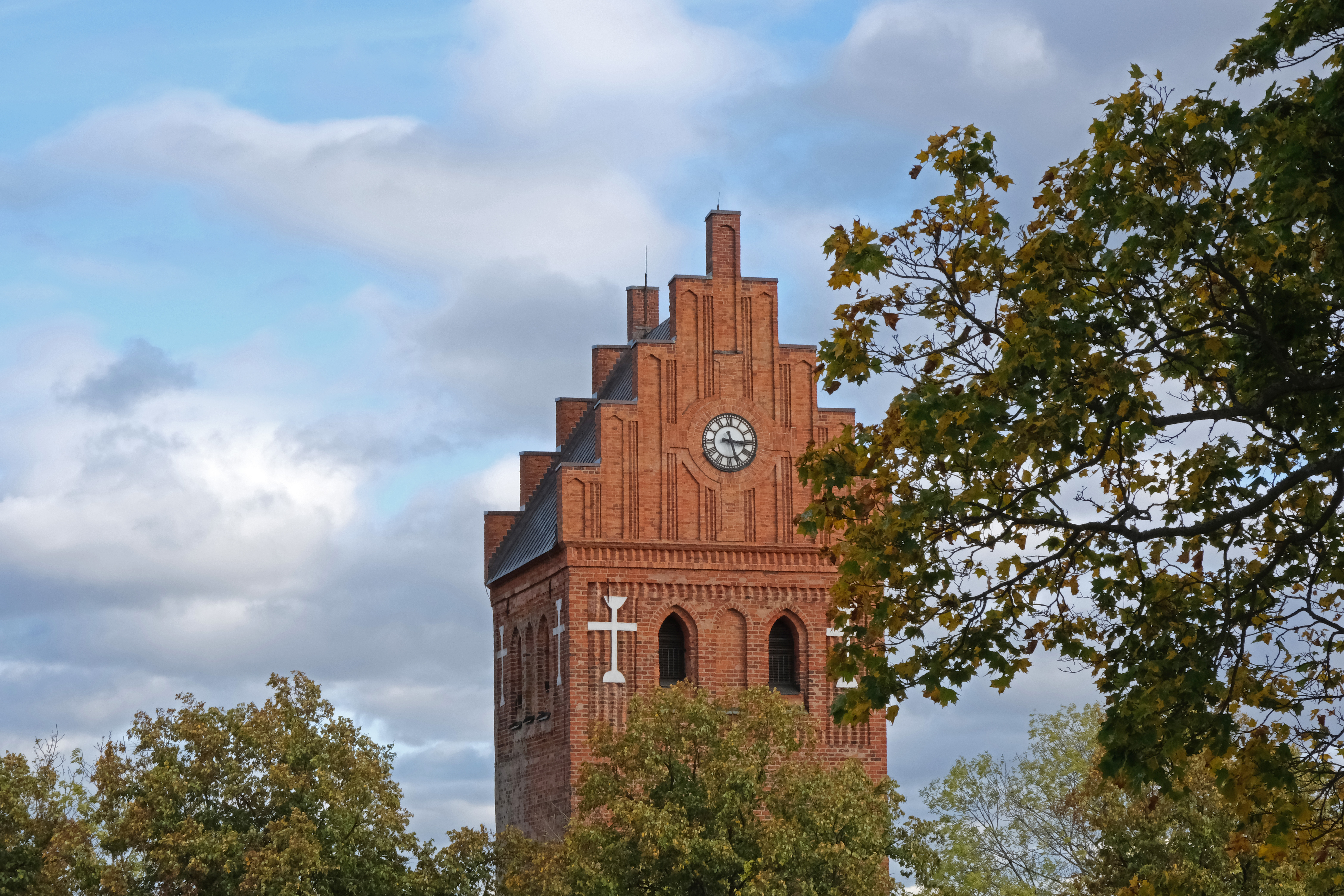 Torshälla kyrktorn. Grenar med höstlöv.