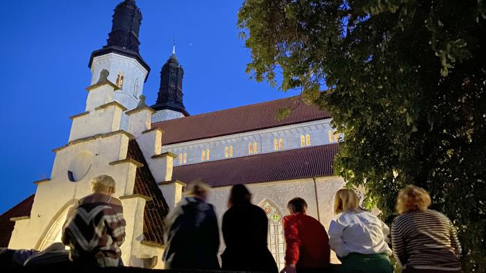 Ungdomar i domkyrkoförsamlingen sitter på en mur och kikar på domkyrkan.