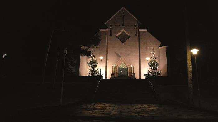 En upplyst Sandvikens kyrka i adventsmörkret.