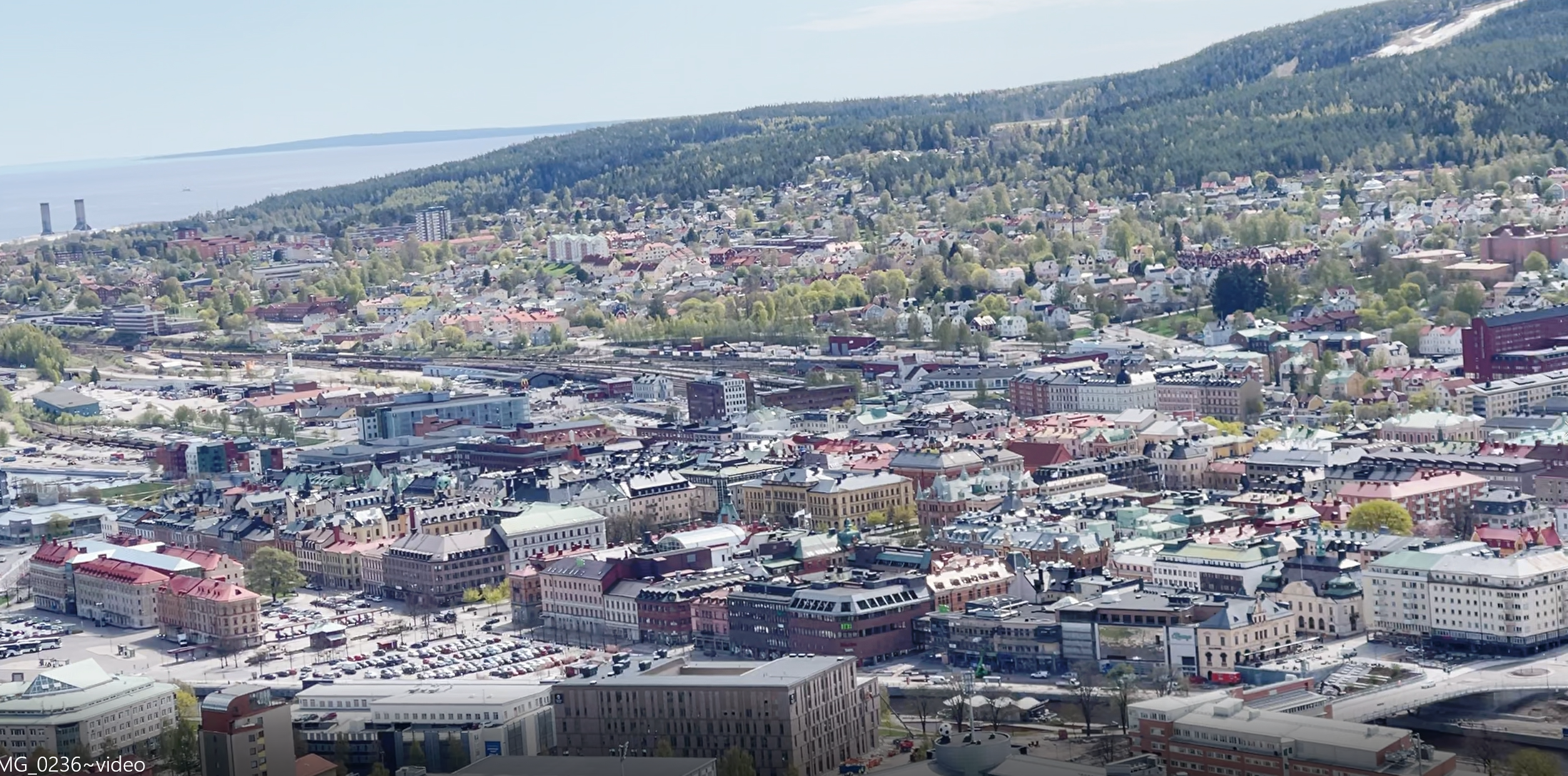 Vy över stad från Sundsvalls norra stadsberg. Byggnader, berg och hav.