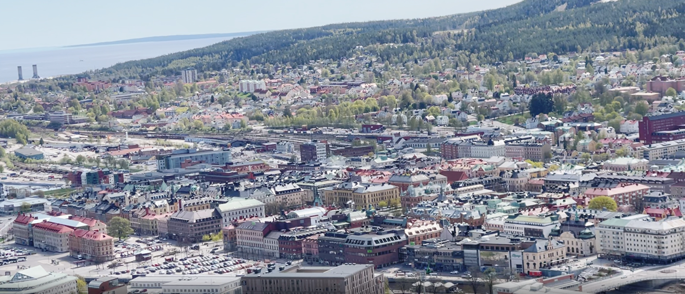 Vy över stad från Sundsvalls norra stadsberg. Byggnader, berg och hav.