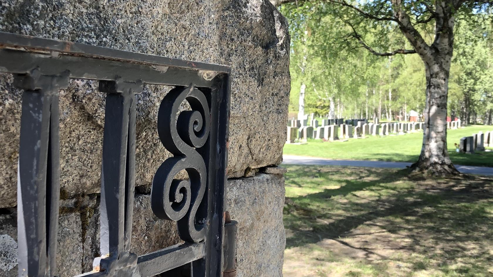 Sten mur med en järngrind som leder in till en grönskande kyrkogård.