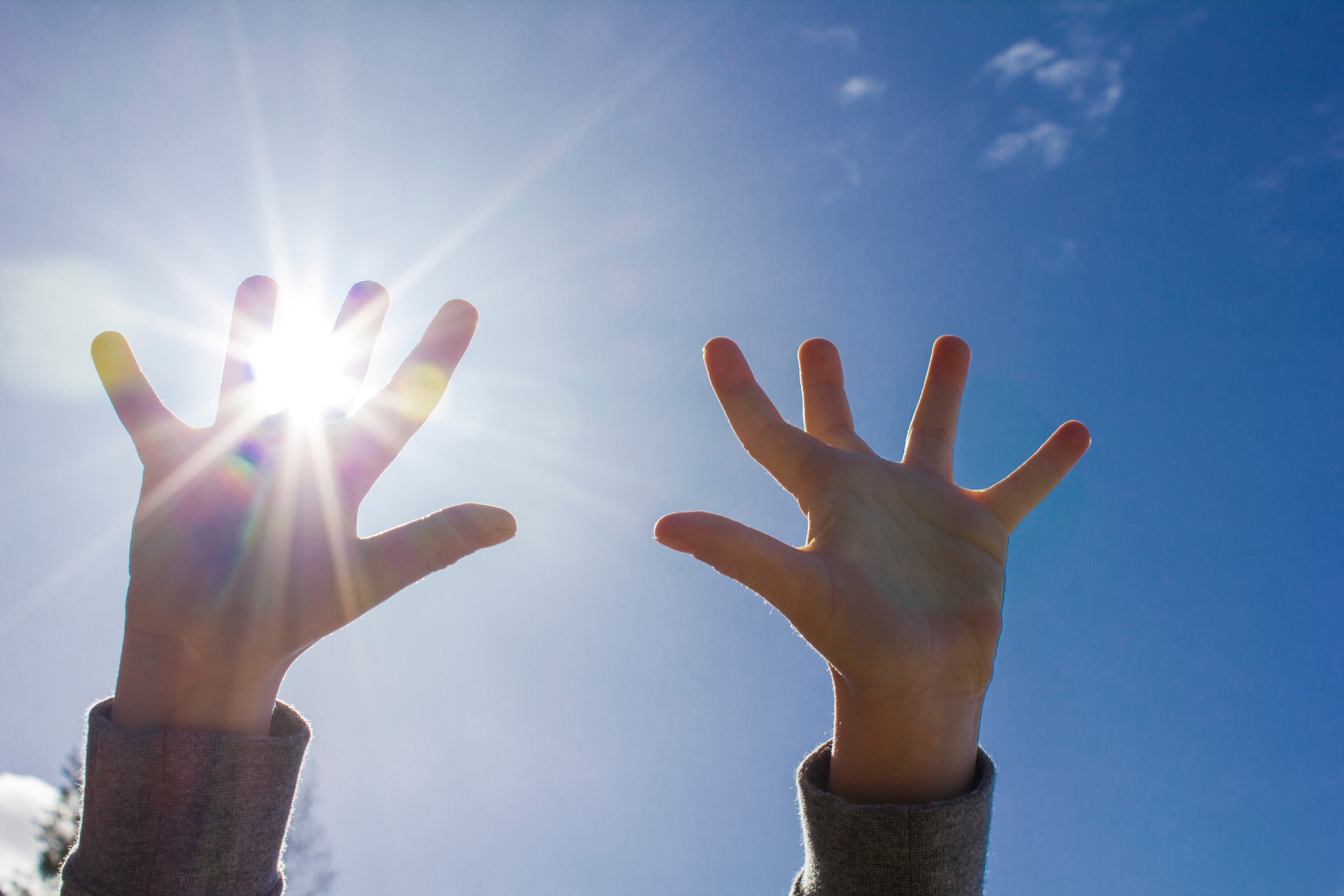 Barnhänder sträckta mot himlen med solstrålar mellan fingrarna.