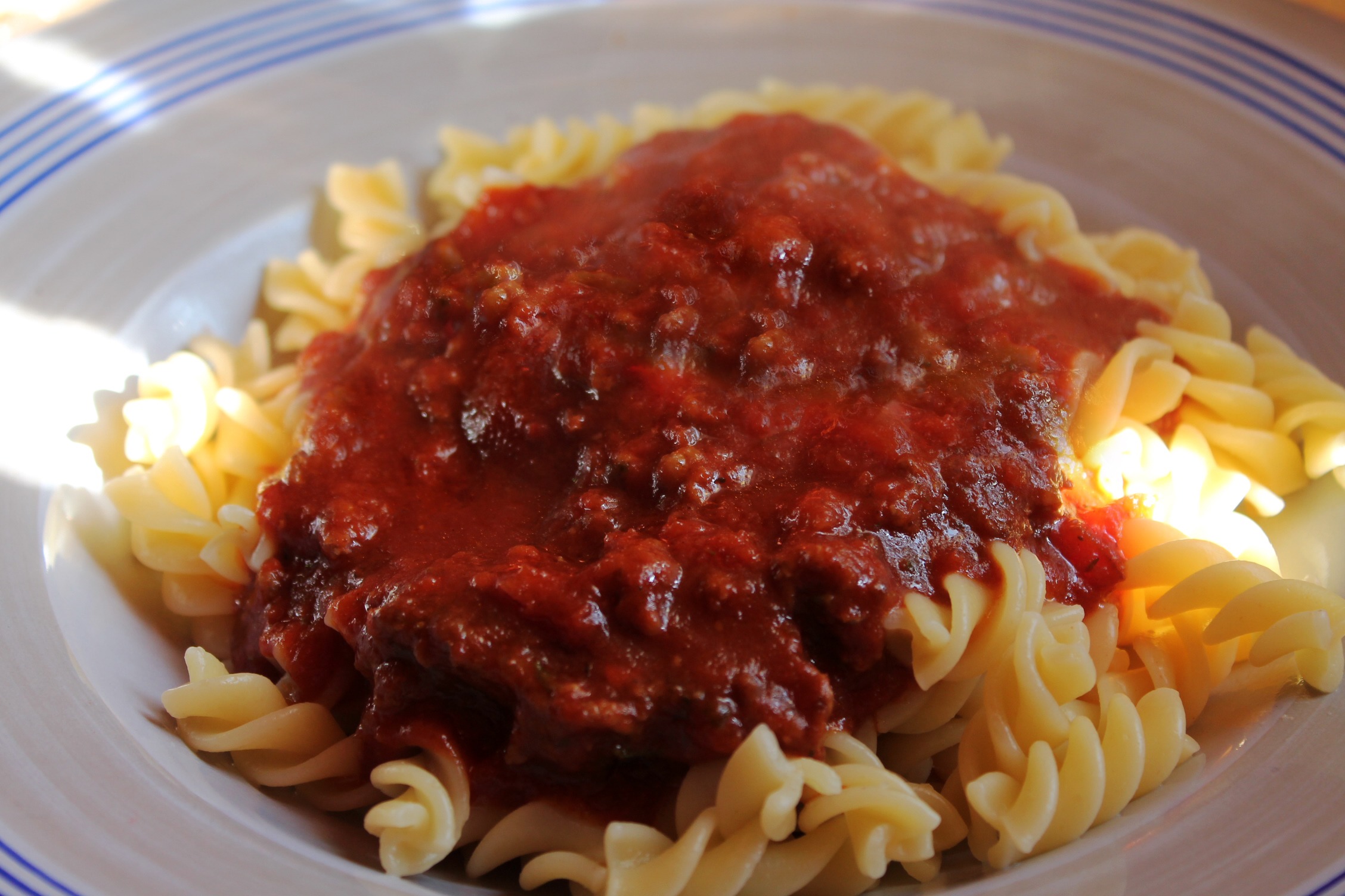 Tallrik med pasta och köttfärssås, belyst av en solstrimma.