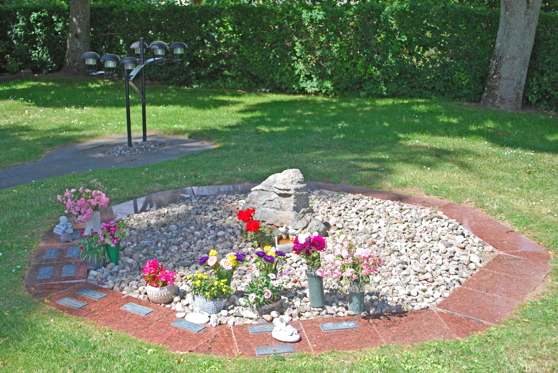 Askgravplatsen på Kverrestads kyrkogård. små röda stenar med namnplatta på och blommor