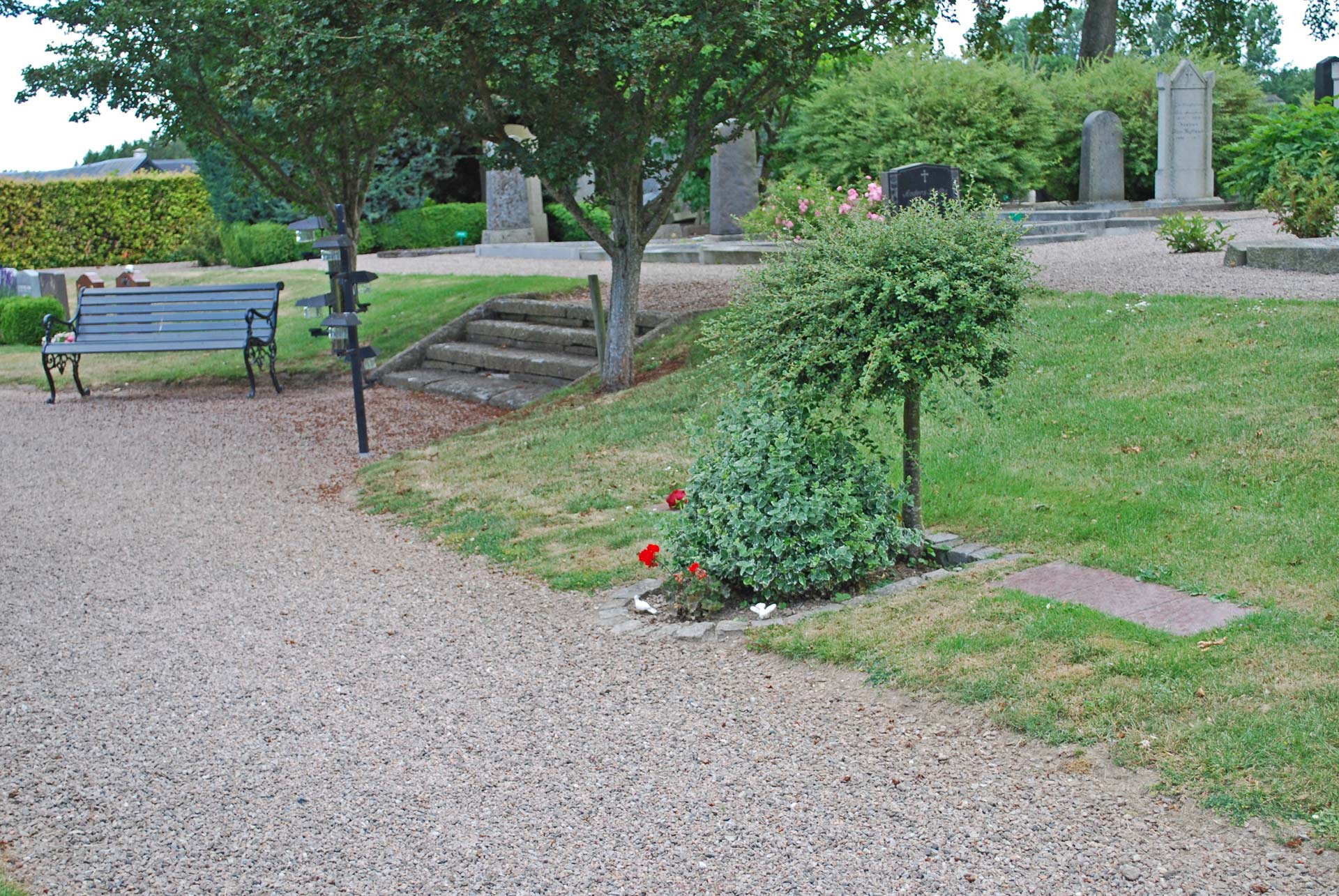 Askgravplatsen på Övraby kyrkogård med bänk att sitta på, ljusbärare och textplattor och buskar