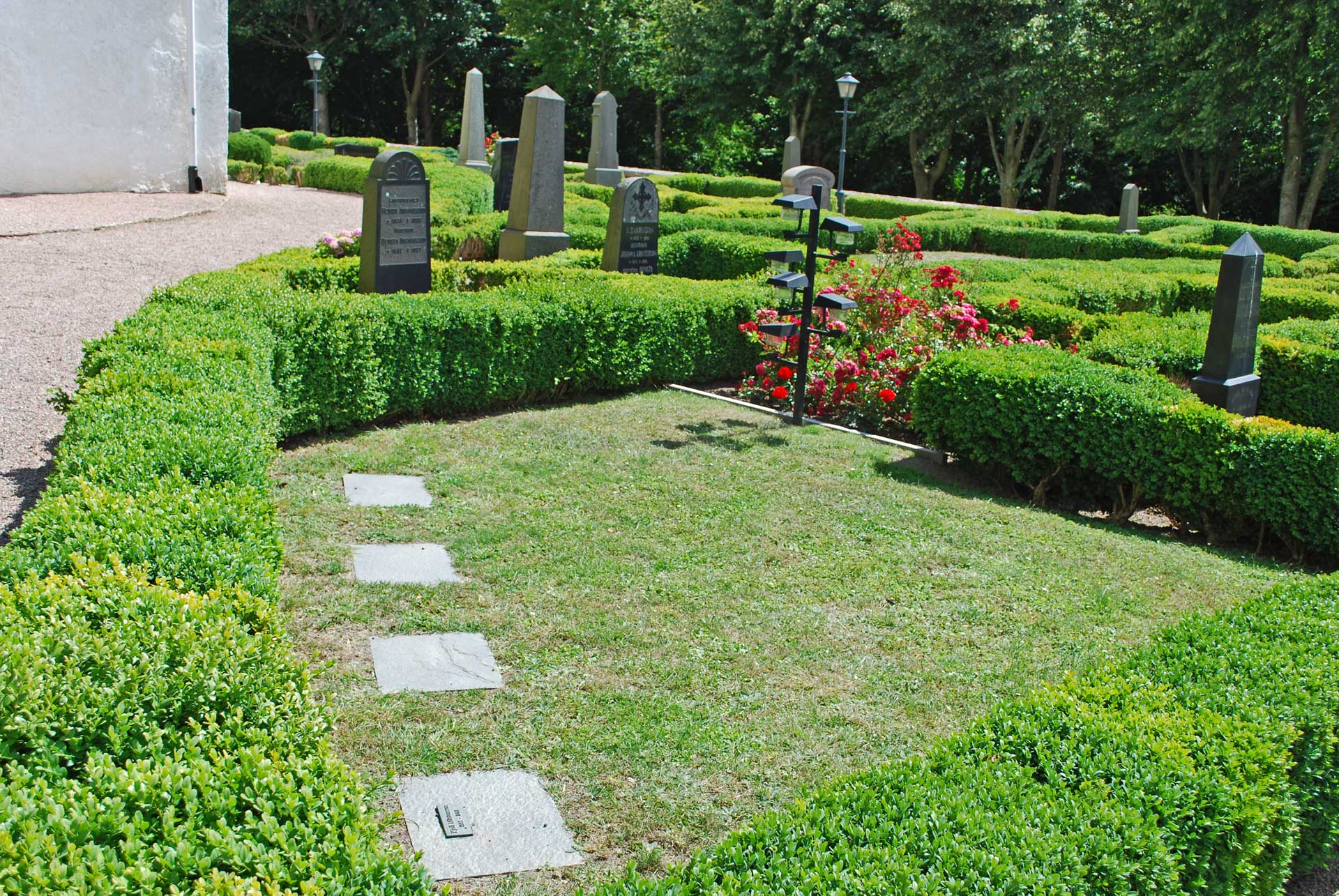 Askgravplatsen på Tosterups kyrkogård, inramad av boxbumshäckar, ljusbärare, blommor och textplattor.ll