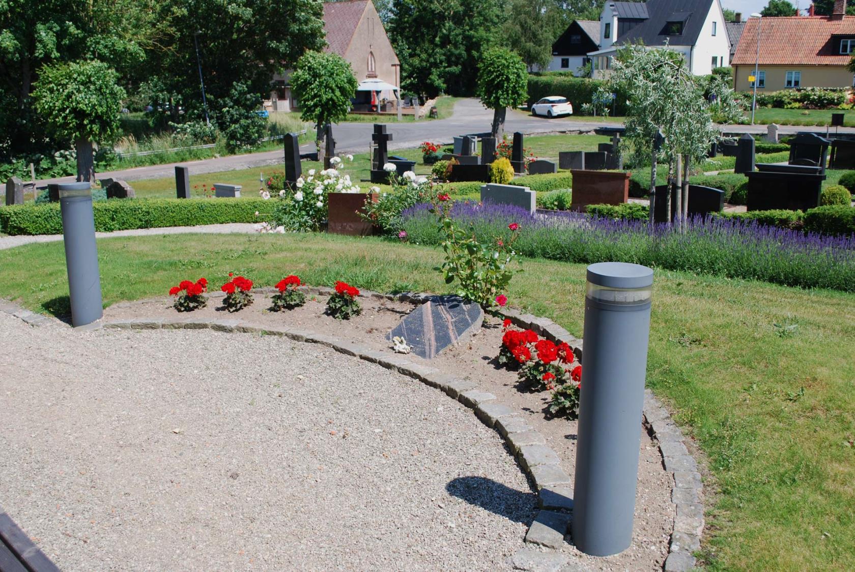 Minneslund Östra Ingelstad med röda pelargoner i rabatten.