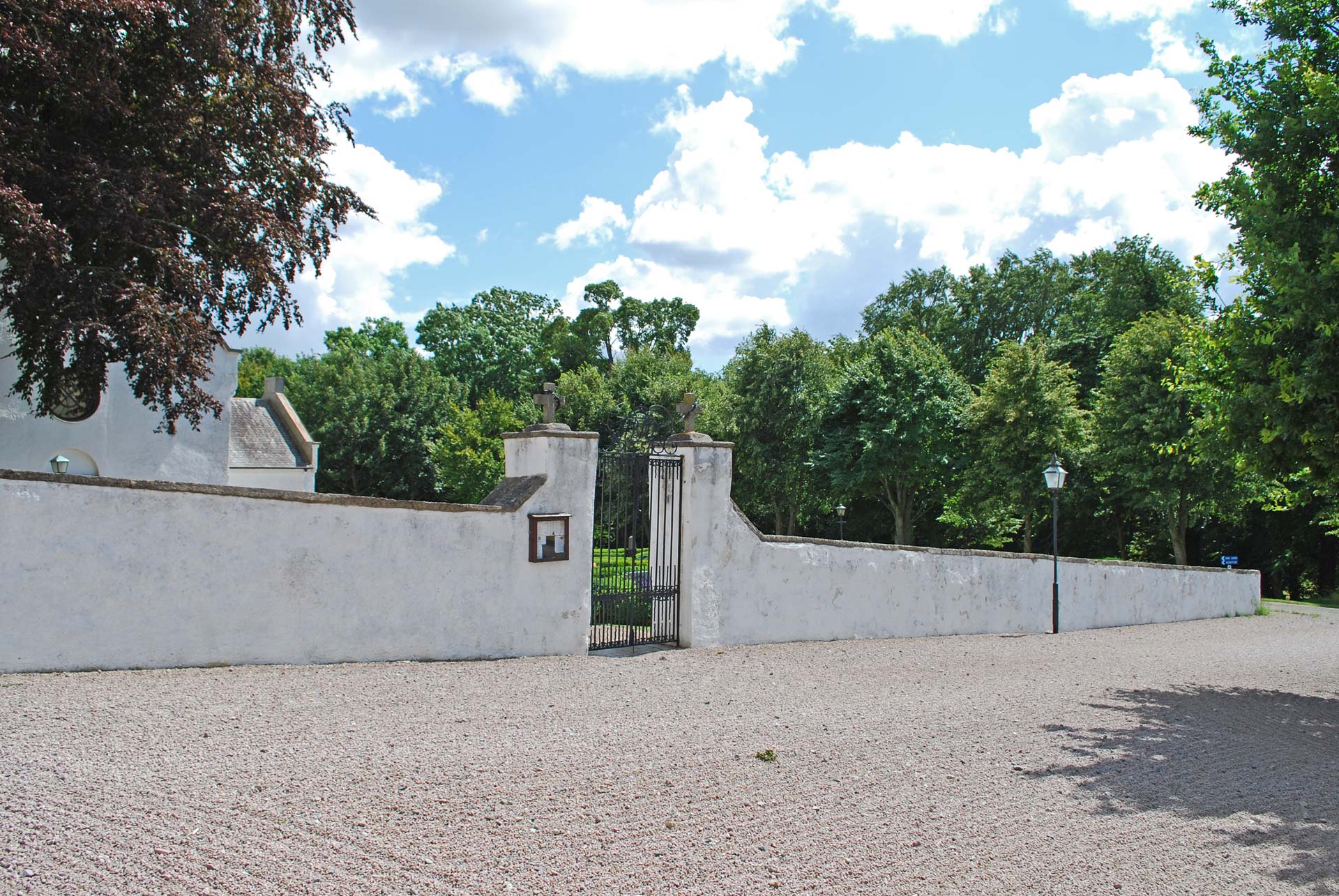Muren vid Tosterups kyrka, vitkalkad mur med svart grind som leder in till kyrkan och kyrkogården