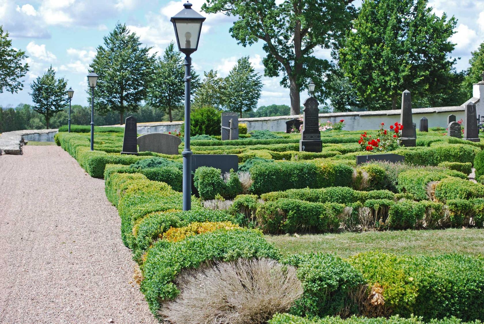 Utsikt över kyrkogården, med gravstenar och buskar och boxbumshäckar