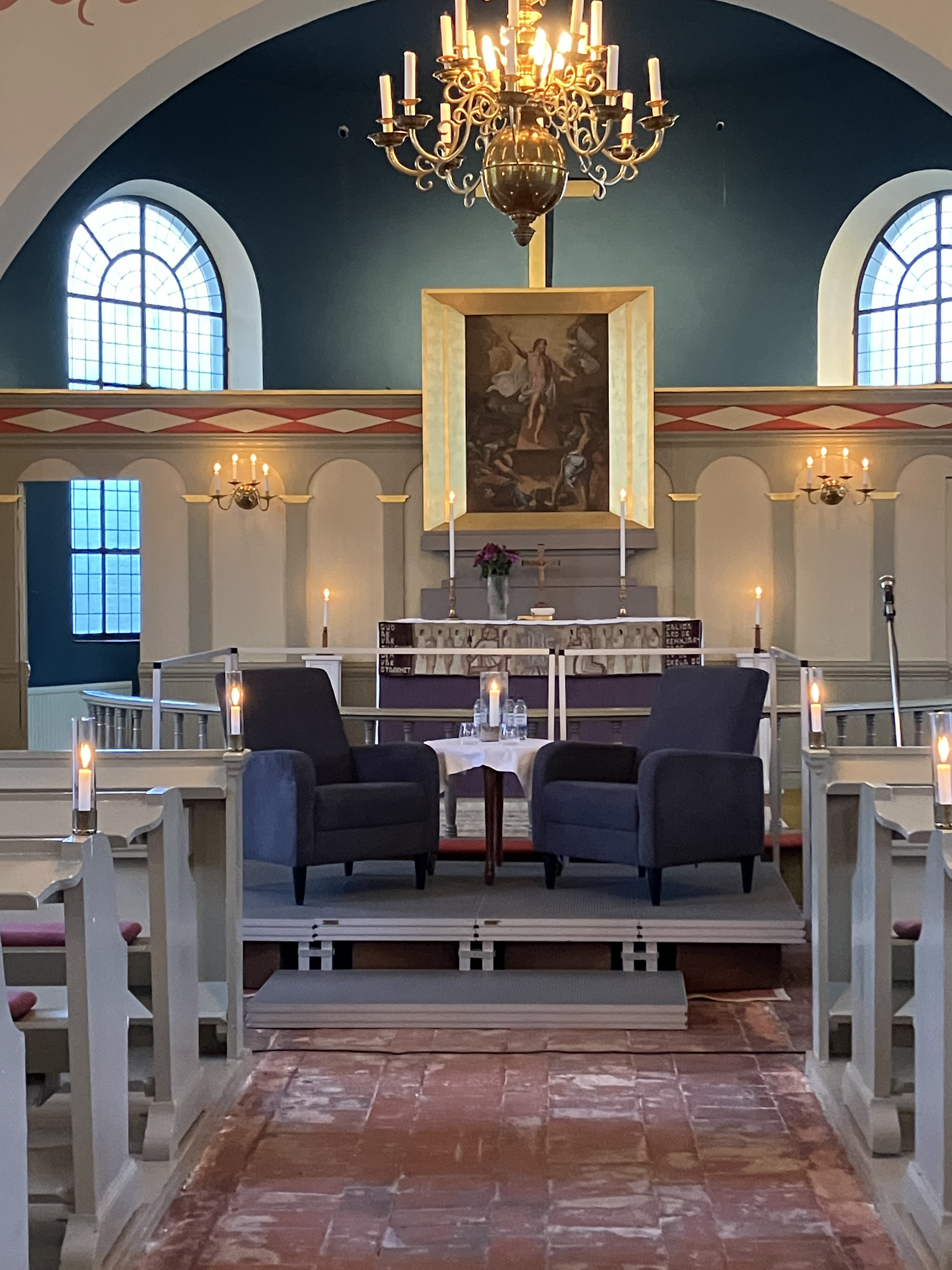 två fåtöljer, altare, kyrka, tända ljus och ljuskrona. 