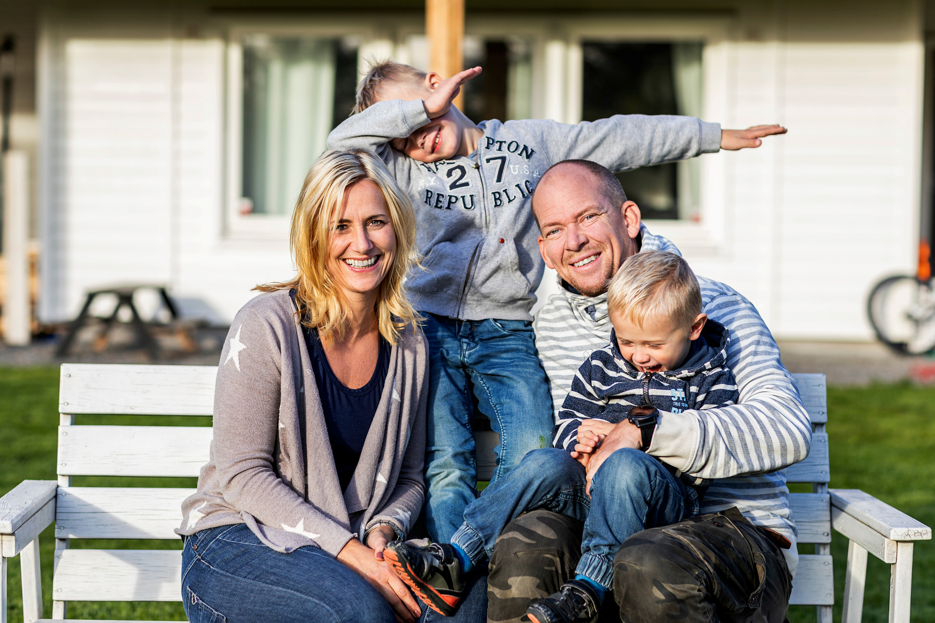 En familj med mamma, pappa och två ganska små barn sitter tätt ihop på en bänk och skrattar.