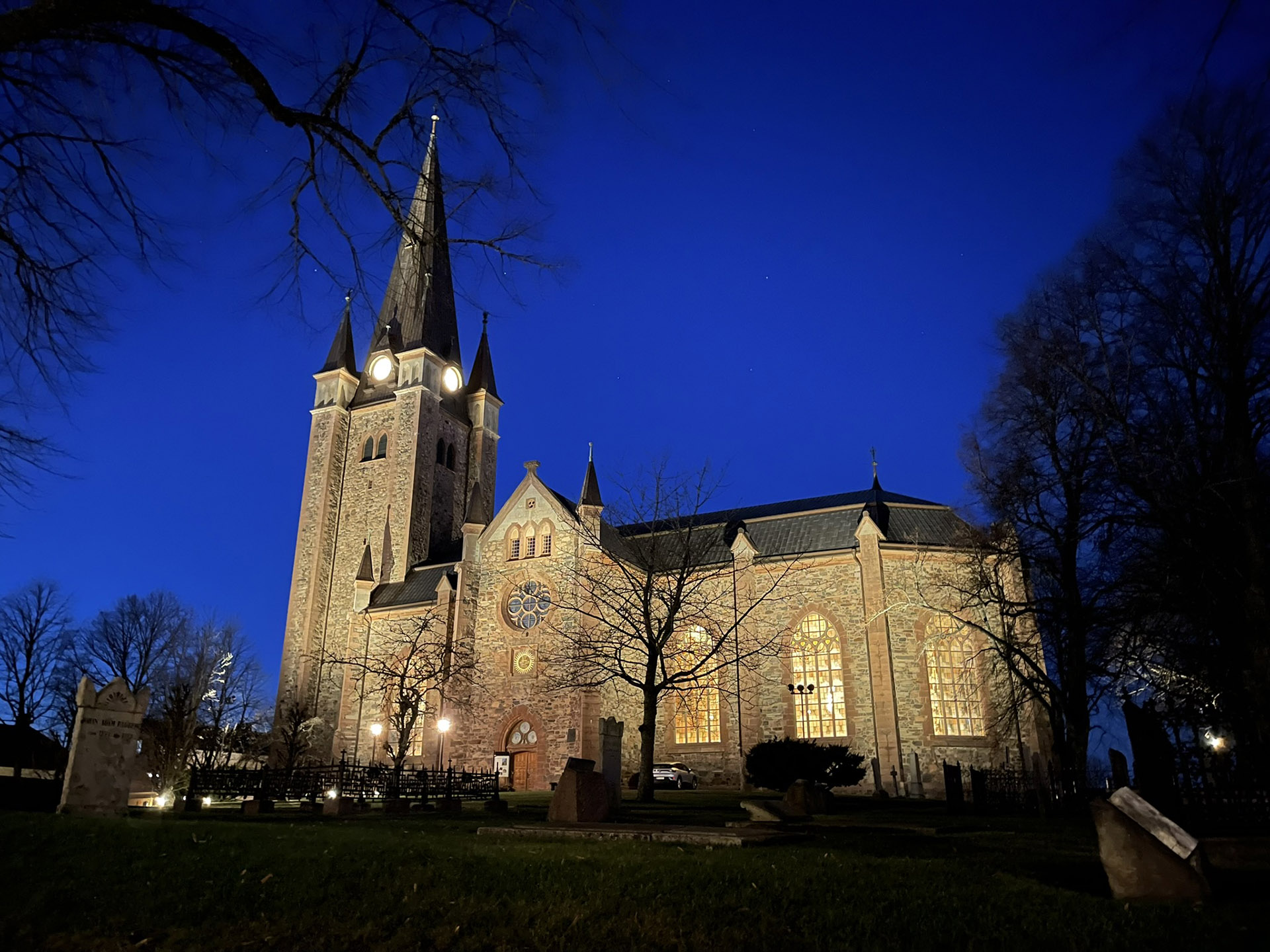 Upplyst stor stenkyrka i rödaktig sten mot en mörkblå natthimmel.