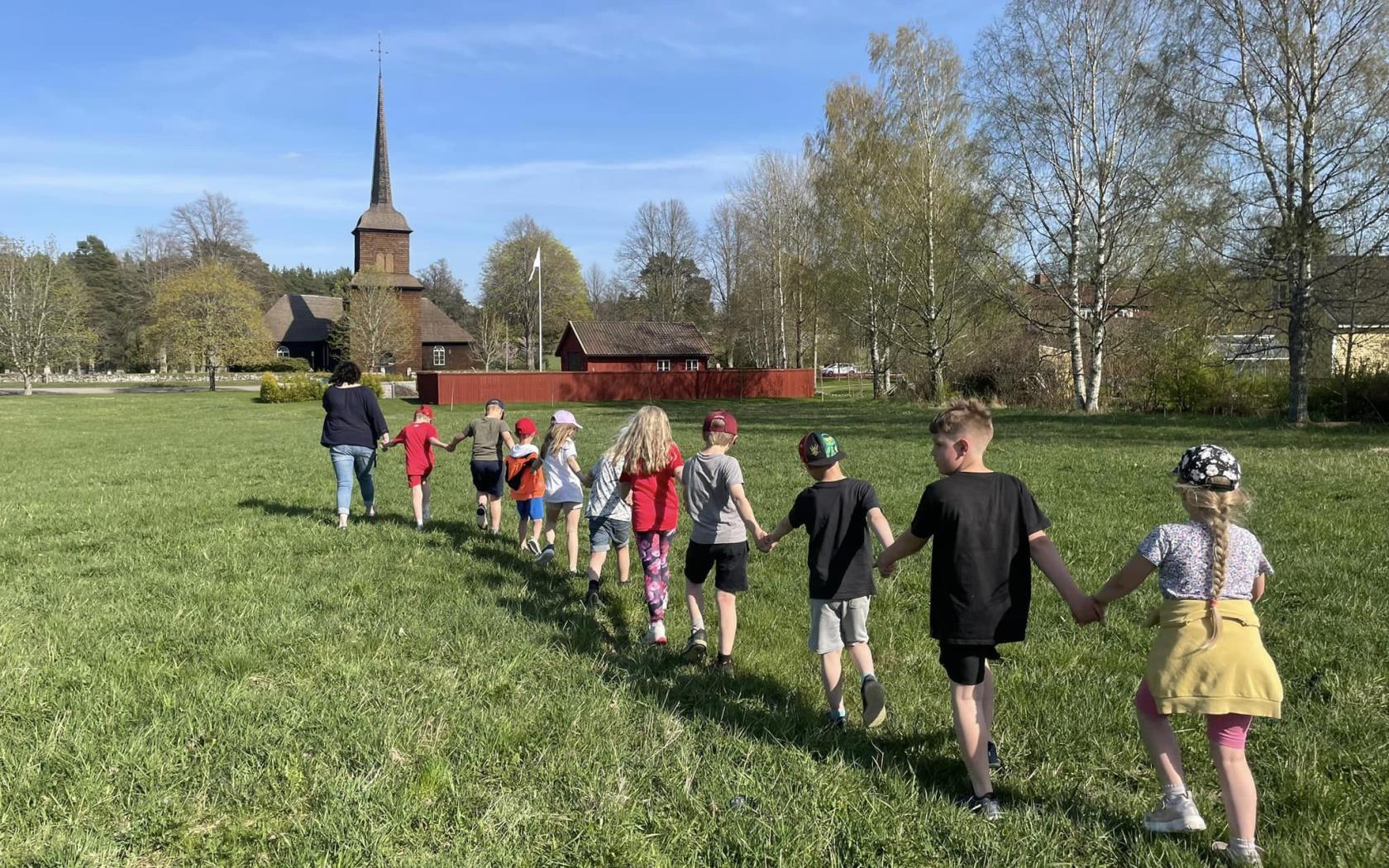 En grupp med barn som går i led och håller hand på en sommaräng