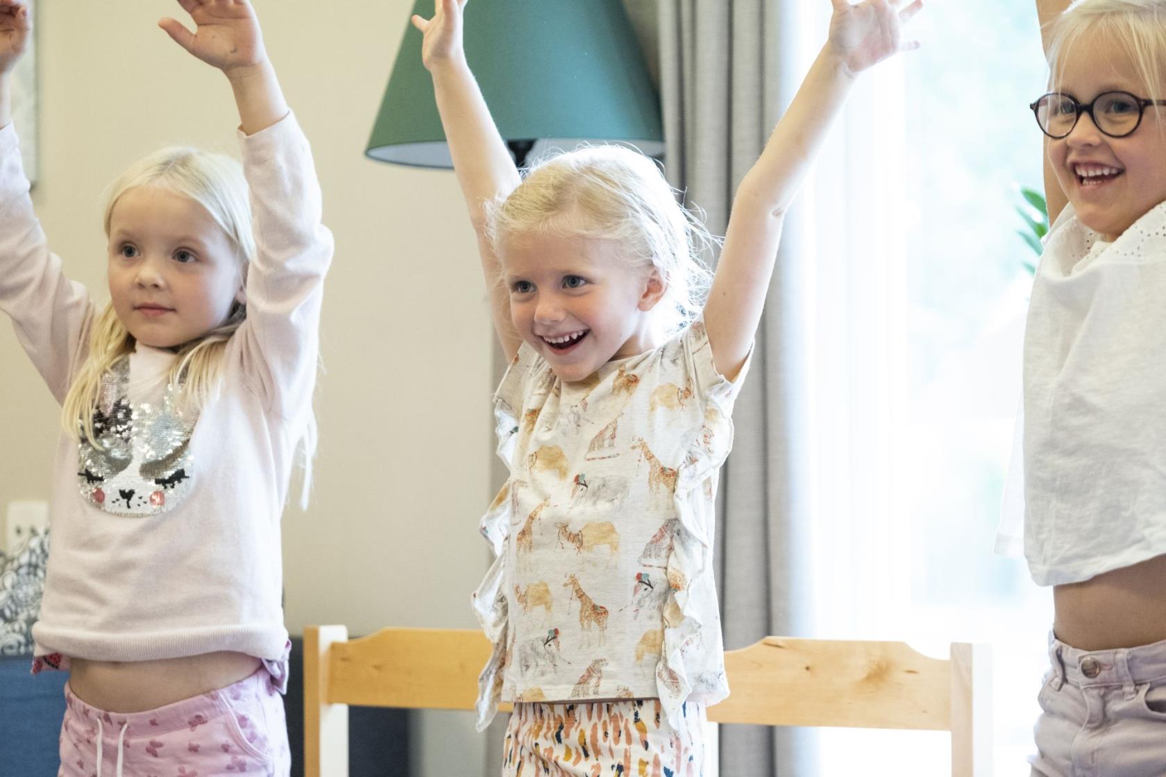 Tre barnkörsbarn står på rad och sträcker upp armarna.