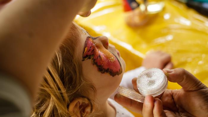Ett barn får en ansiktsmålning med färg och glitter.