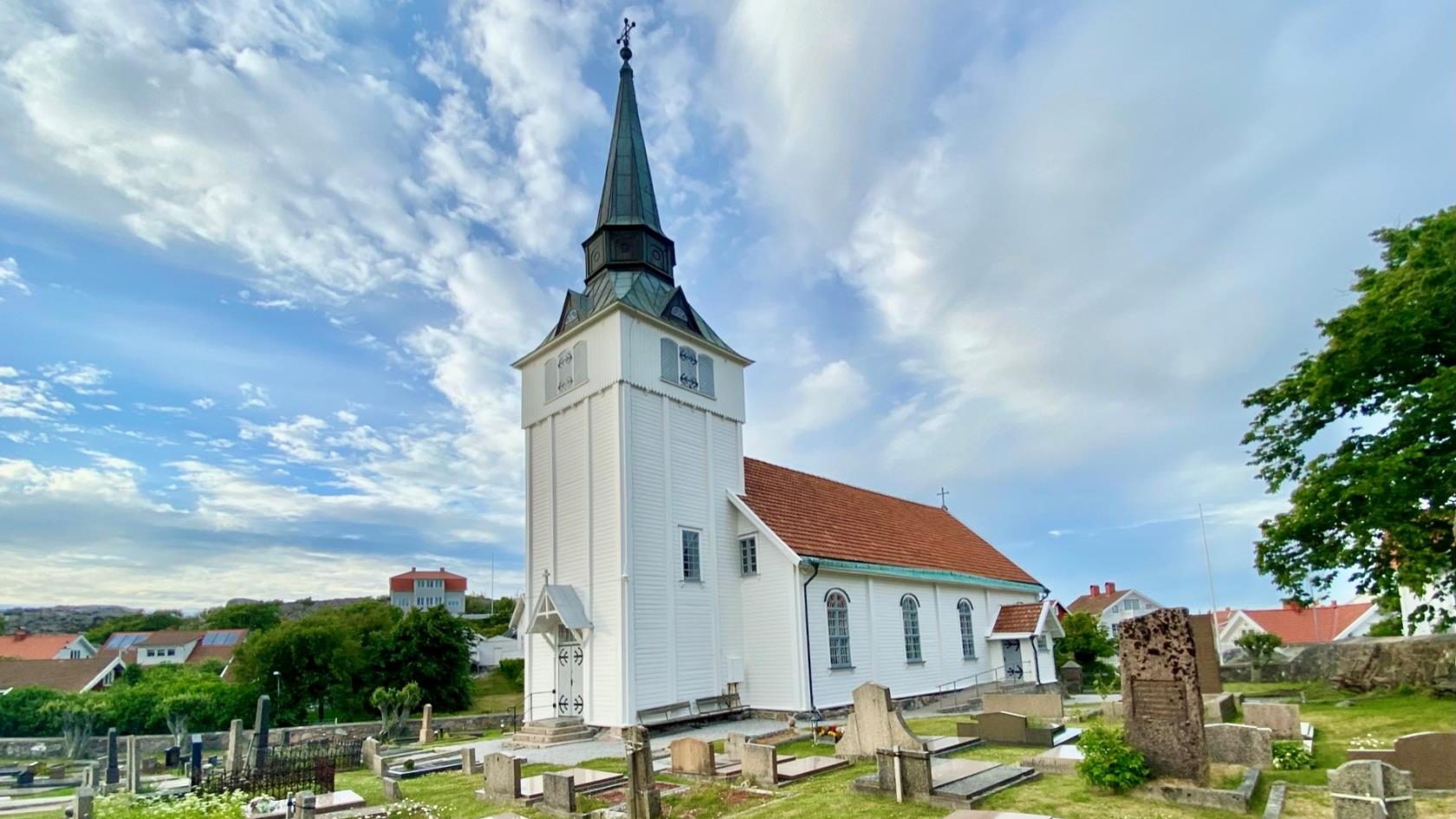 Gullholmens kyrka. På himlen bakom sveper vita moln förbi klarblå himmel.