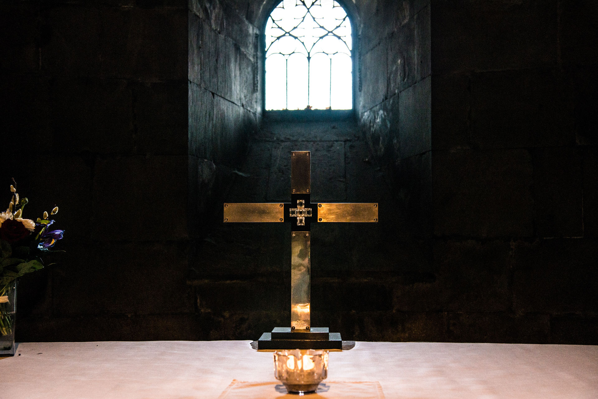 – Kors på altaret i kryptan. Framför korset lyser ett ljus och bakom ett fönster.
