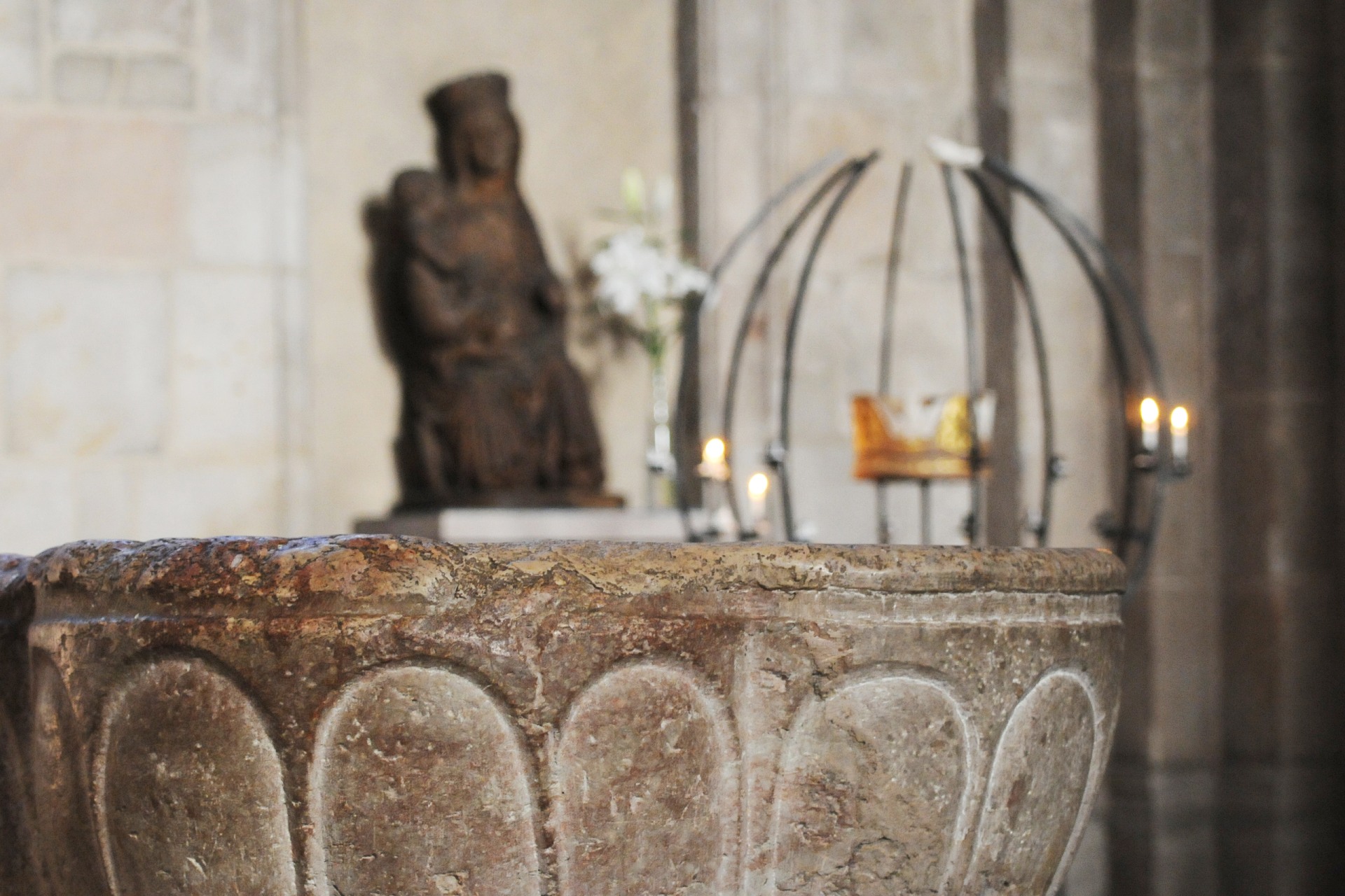 Dopfunt i sten. I bakgrunden syns en ljusbärare och en madonnastaty.